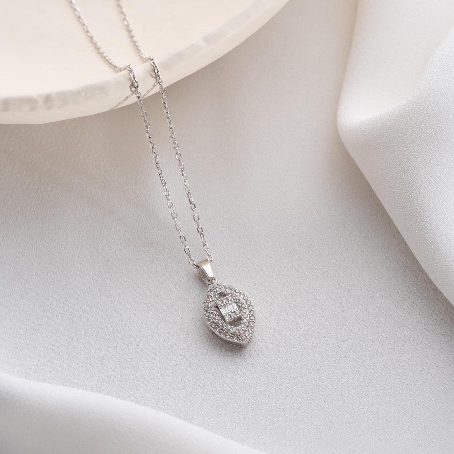 Elegant oval pendant necklace with cubic zirconia stones, available in 925 sterling silver and 14K gold plated options, displayed on a white satin background.