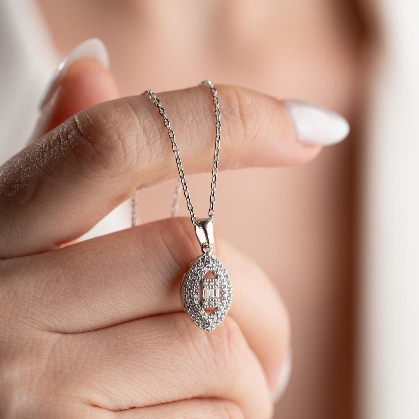 Elegant oval pendant necklace with cubic zirconia stones, available in 925 sterling silver and 14K gold plated options, displayed on a white satin background.