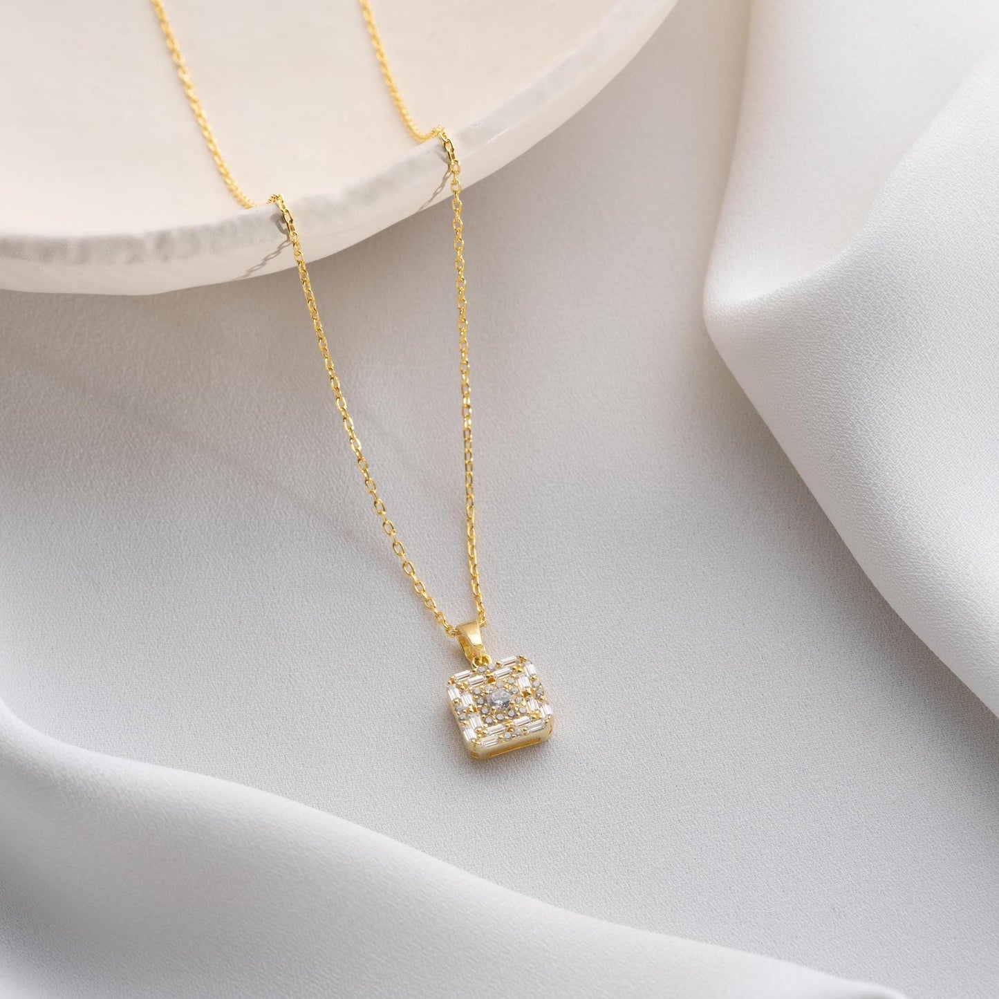 Square pendant necklace with cubic zirconia stones, available in 925 sterling silver and 14K gold plated options, displayed on a white satin background.