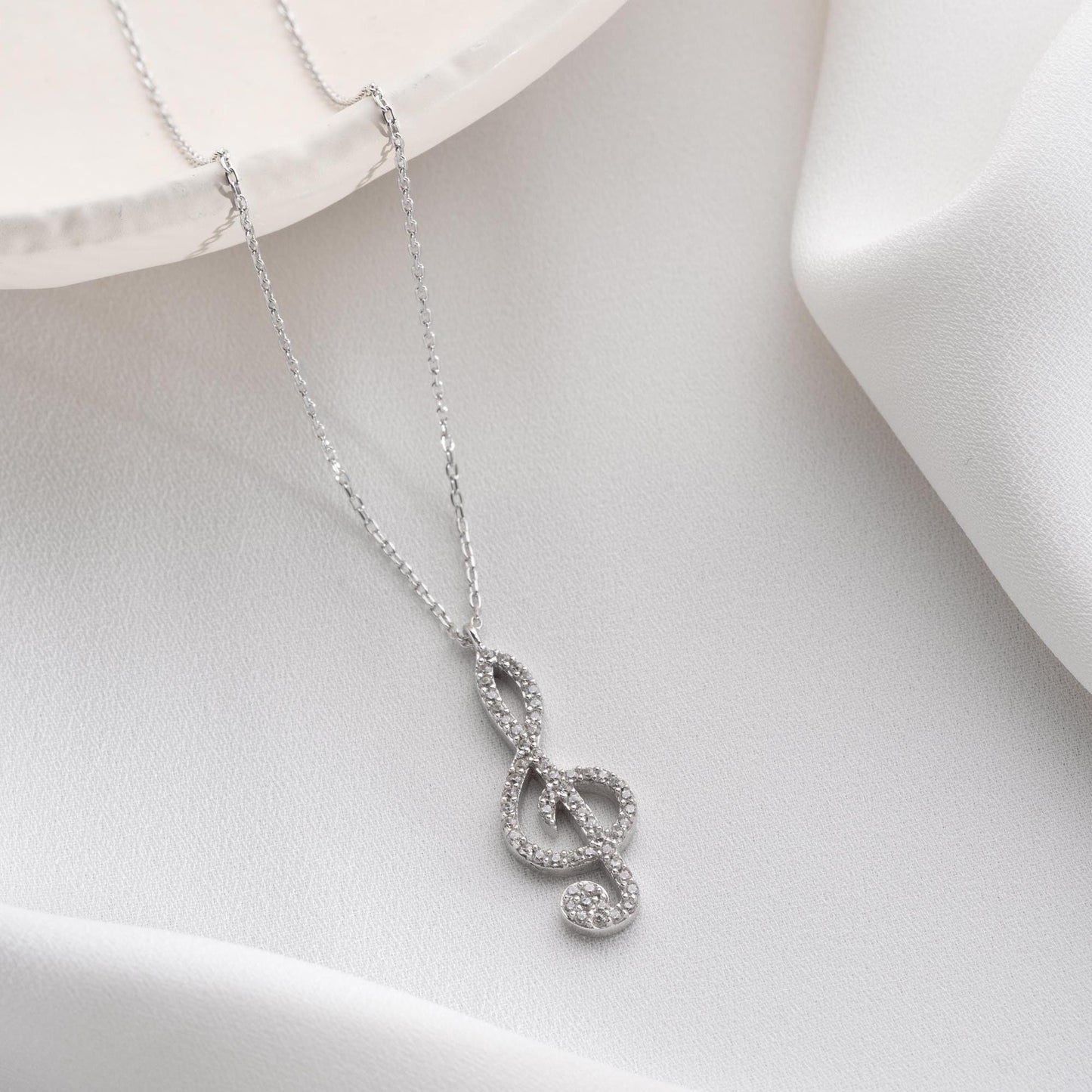 Music note necklace with cubic zirconia stones, available in 925 sterling silver and 14K gold plated options, displayed on a white satin background.