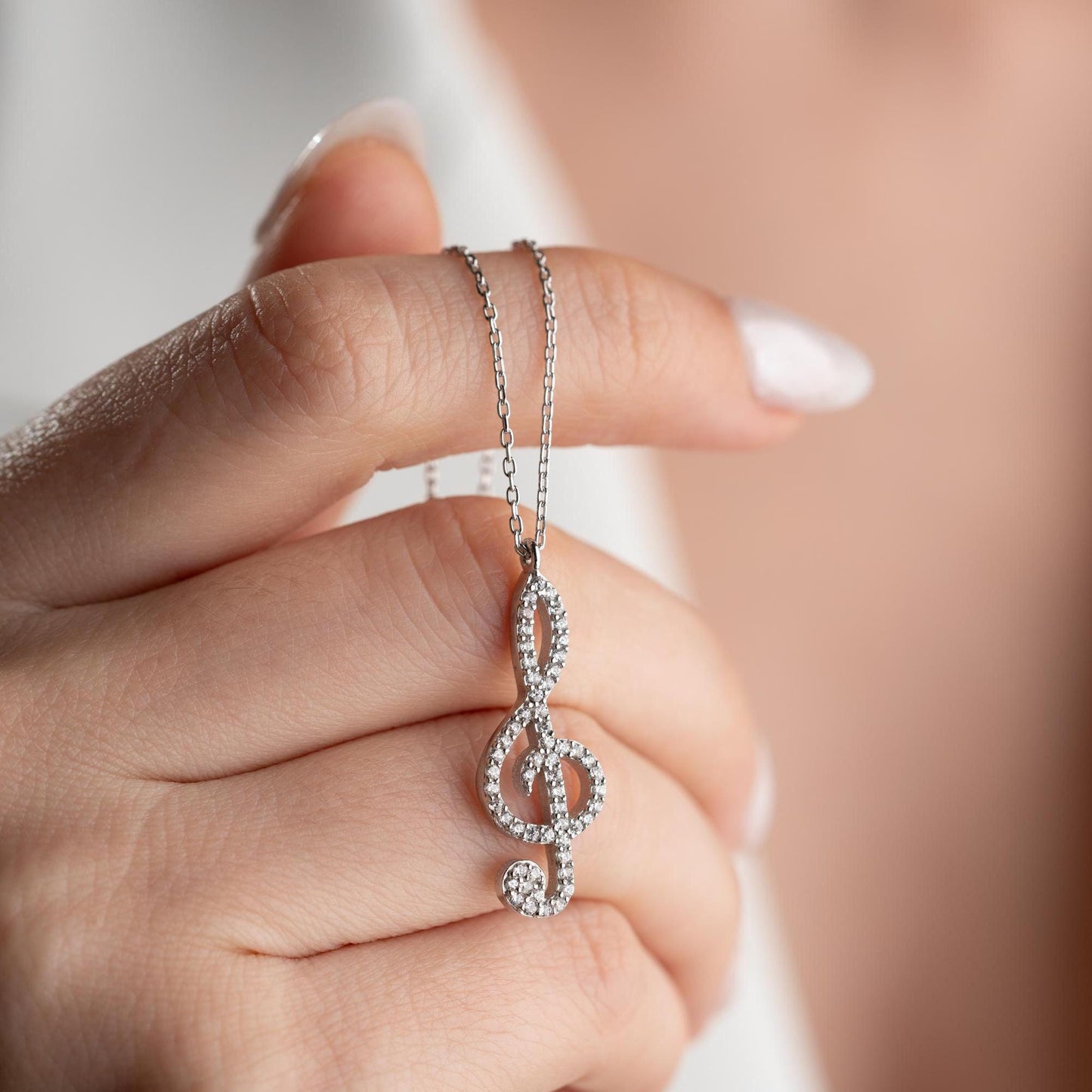 Music note necklace with cubic zirconia stones, available in 925 sterling silver and 14K gold plated options, displayed on a white satin background.