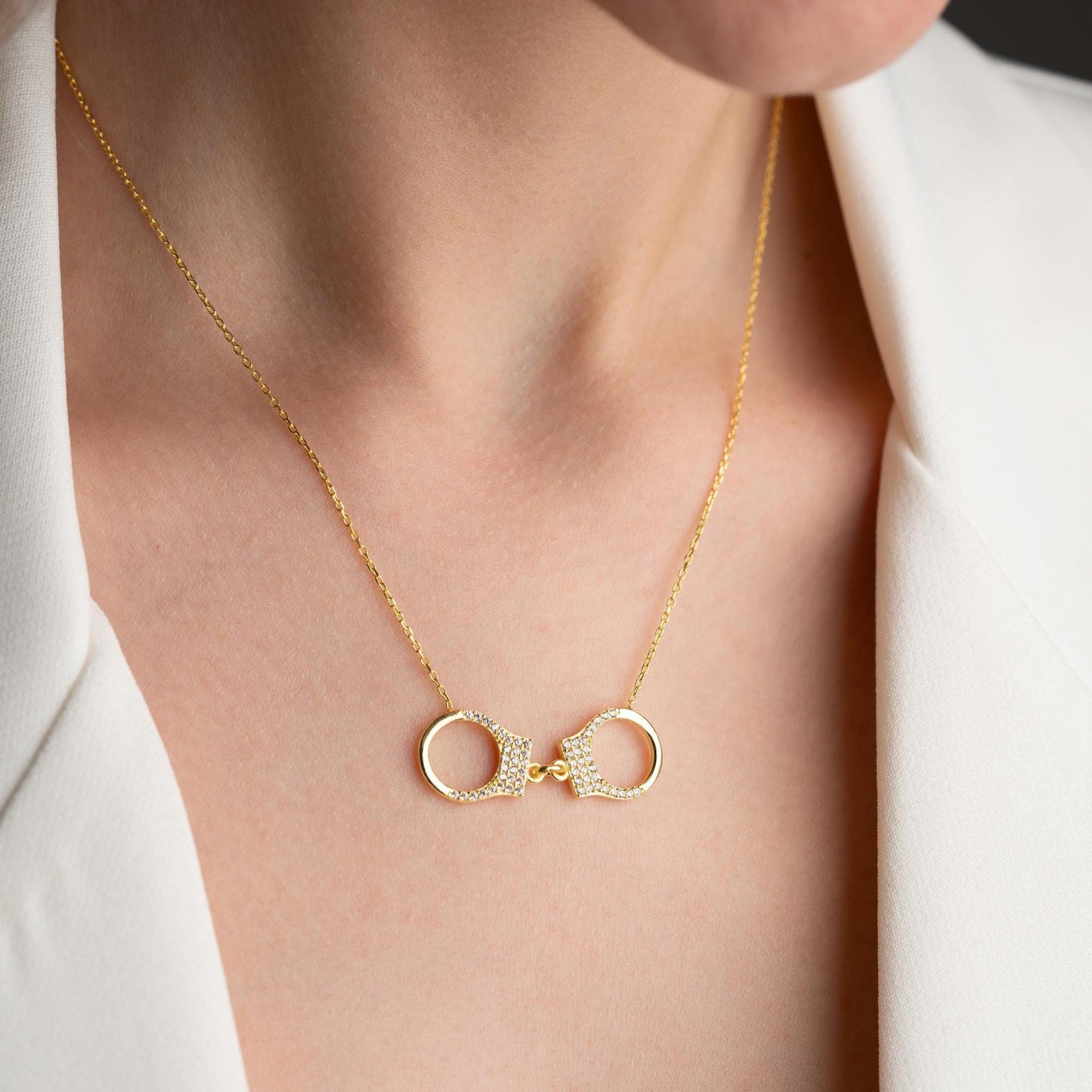 Handcuff necklace with cubic zirconia stones, available in 925 sterling silver and 14K gold plated options, displayed on a white satin background.