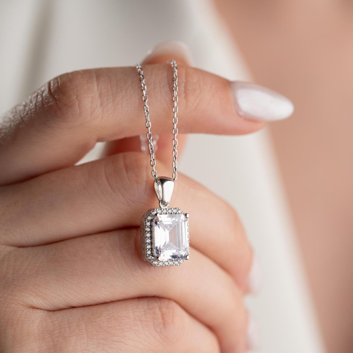 Emerald-cut pendant necklace with cubic zirconia stones, available in 925 sterling silver and 14K gold plated options, displayed on a white satin background.