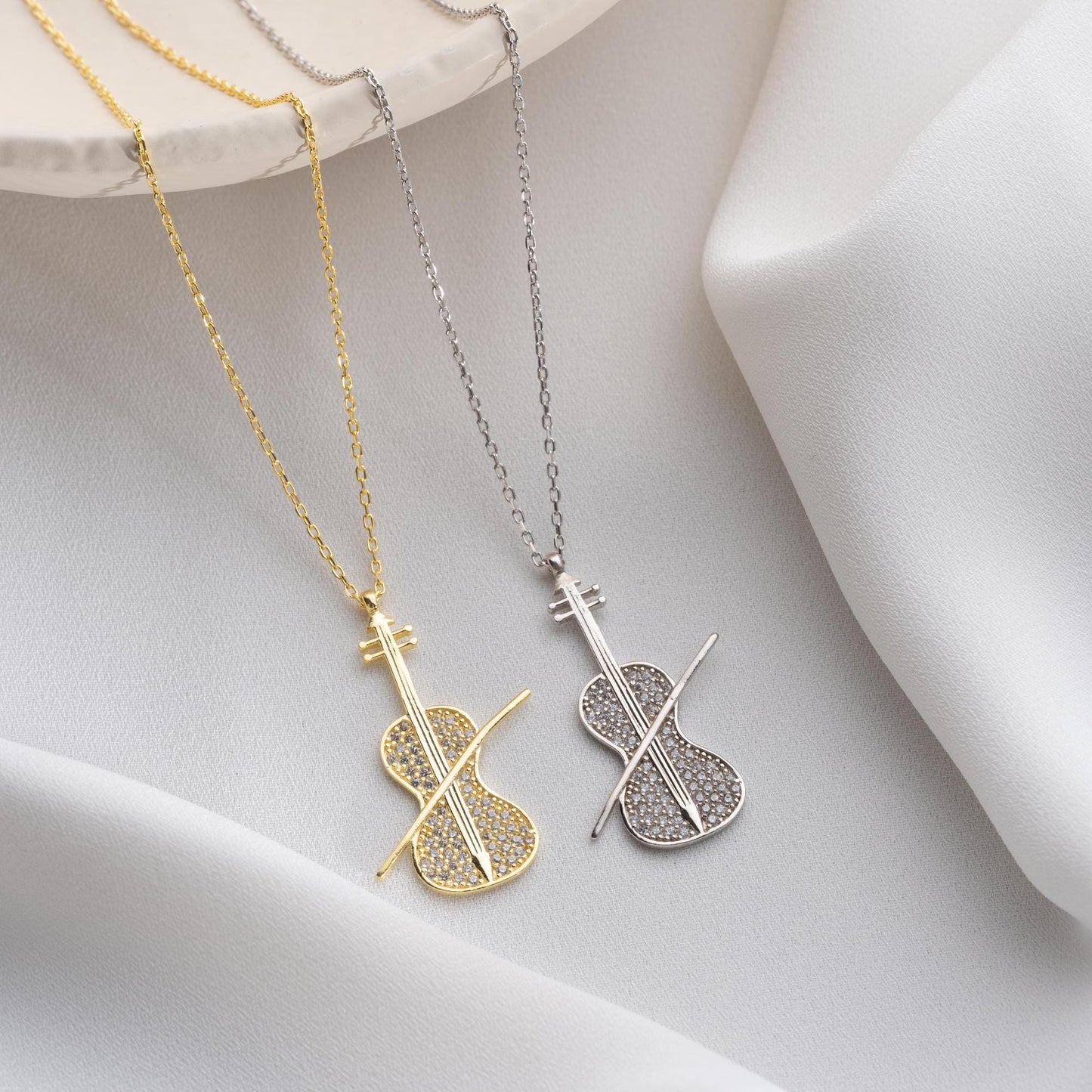 Violin-shaped necklace with cubic zirconia stones, available in 925 sterling silver and 14K gold plated options, displayed on a white satin background.