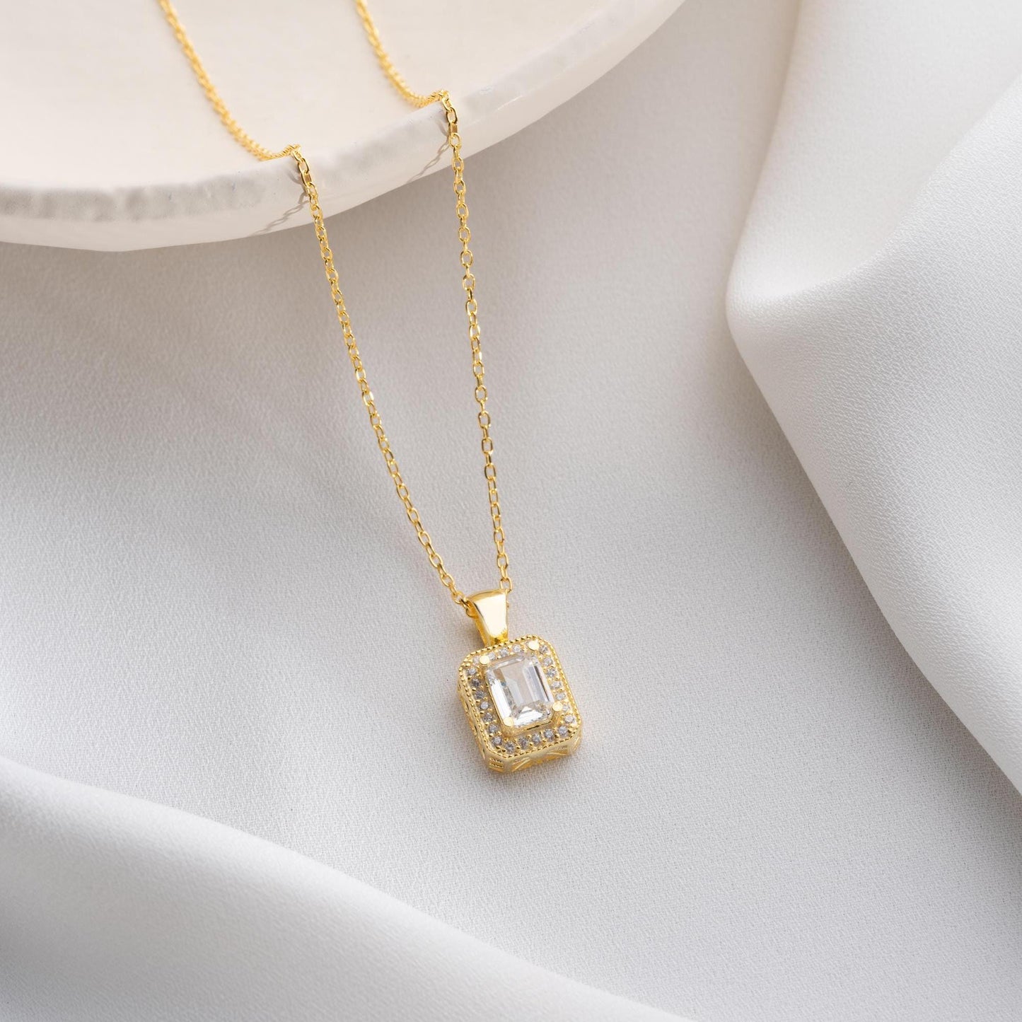 Baguette-cut pendant necklace with cubic zirconia stones, available in 925 sterling silver and 14K gold plated options, displayed on a white satin background