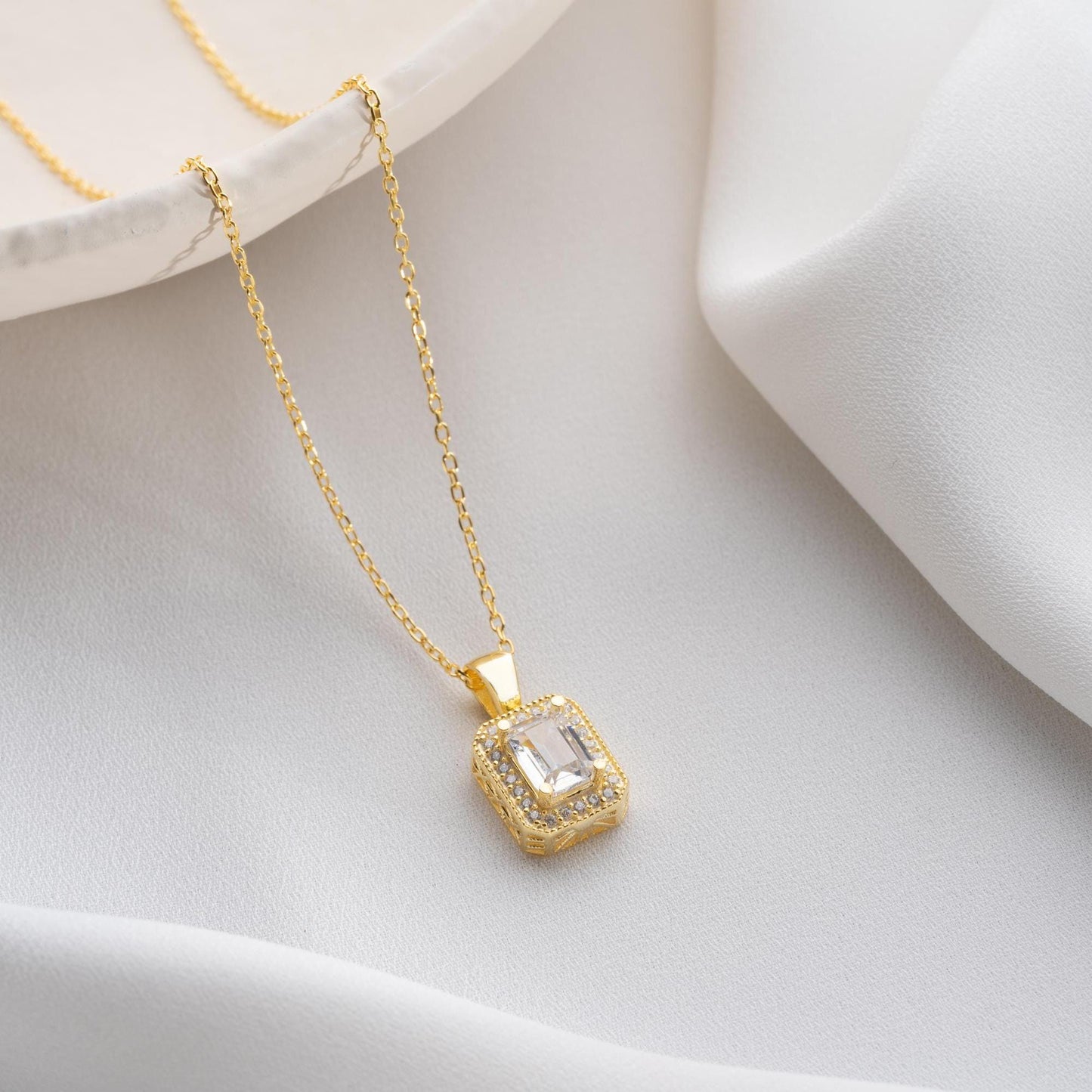 Baguette-cut pendant necklace with cubic zirconia stones, available in 925 sterling silver and 14K gold plated options, displayed on a white satin background