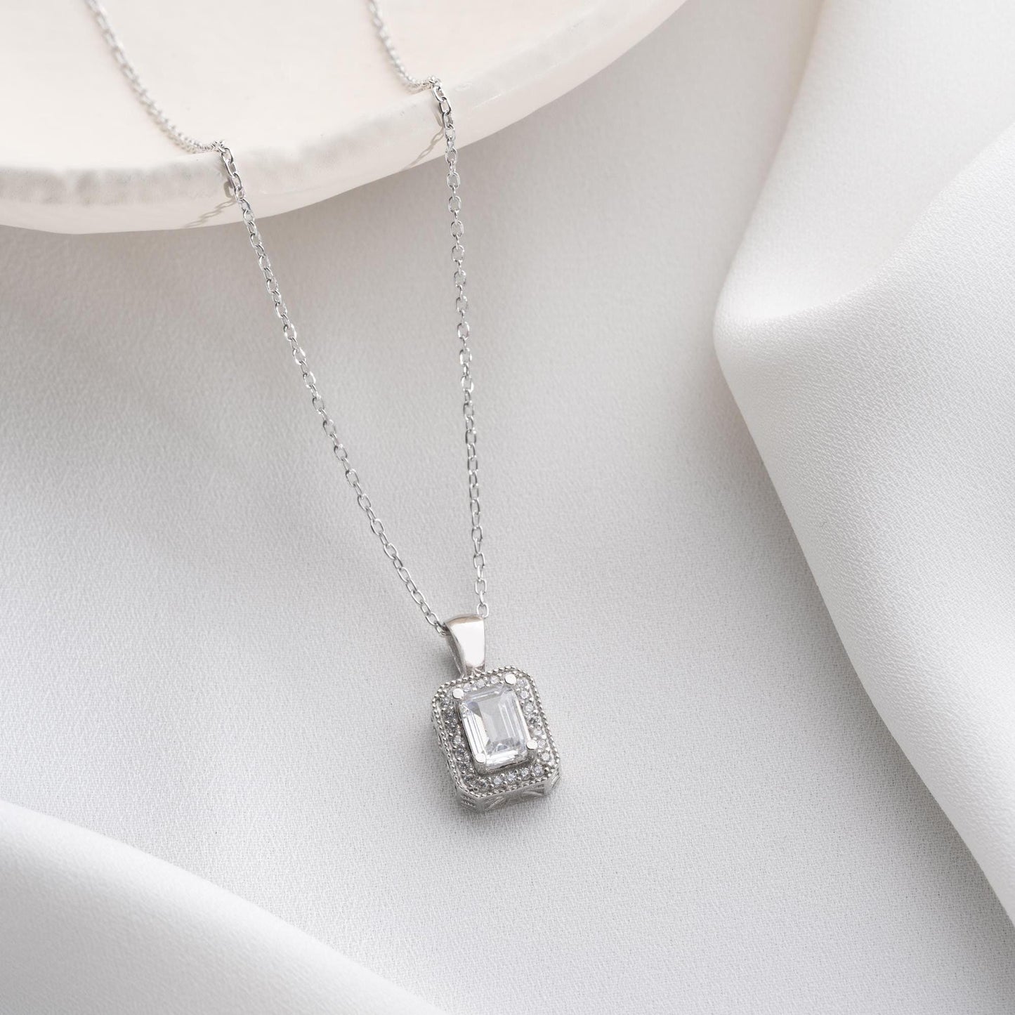 Baguette-cut pendant necklace with cubic zirconia stones, available in 925 sterling silver and 14K gold plated options, displayed on a white satin background