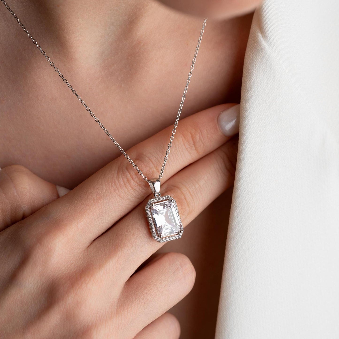 Emerald-cut pendant necklace with cubic zirconia stones, available in 925 sterling silver and 14K gold plated options, displayed on a white satin background