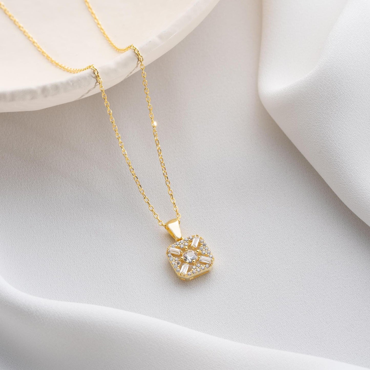 Square pendant necklace with cubic zirconia stones, available in 925 sterling silver and 14K gold plated options, displayed on a white satin background