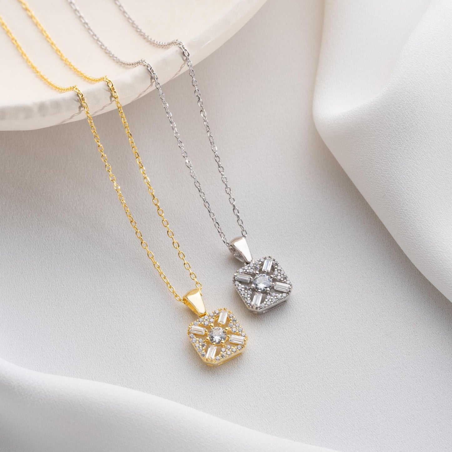 Square pendant necklace with cubic zirconia stones, available in 925 sterling silver and 14K gold plated options, displayed on a white satin background