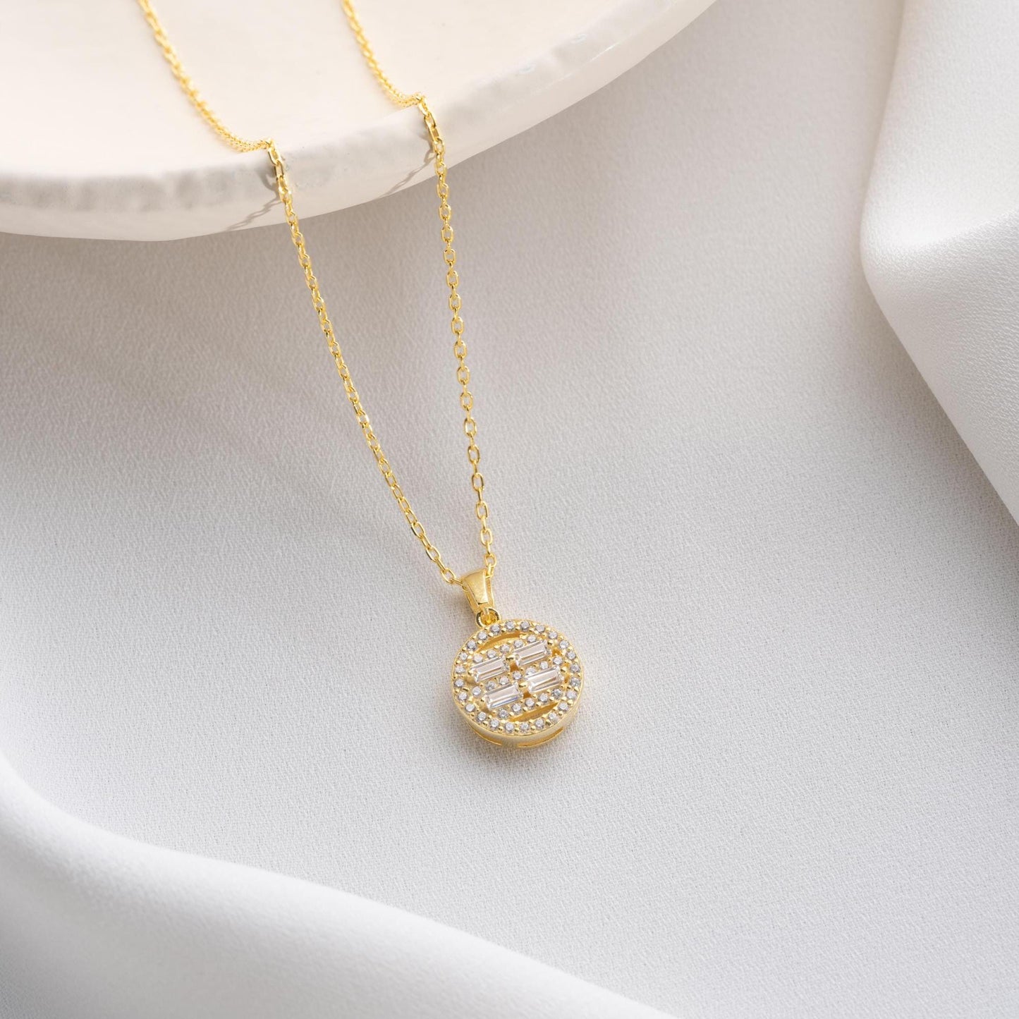 Round pendant necklace with cubic zirconia stones, available in 925 sterling silver and 14K gold plated options, displayed on a white satin background.