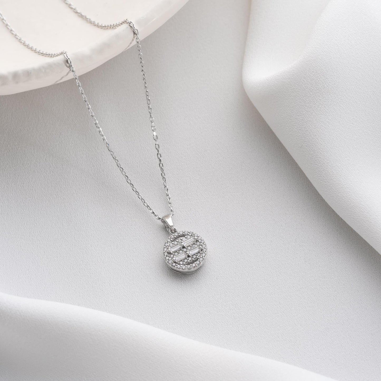 Round pendant necklace with cubic zirconia stones, available in 925 sterling silver and 14K gold plated options, displayed on a white satin background.