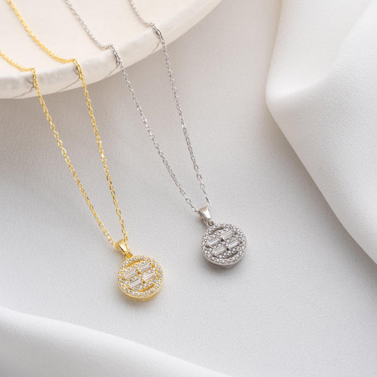 Round pendant necklace with cubic zirconia stones, available in 925 sterling silver and 14K gold plated options, displayed on a white satin background.