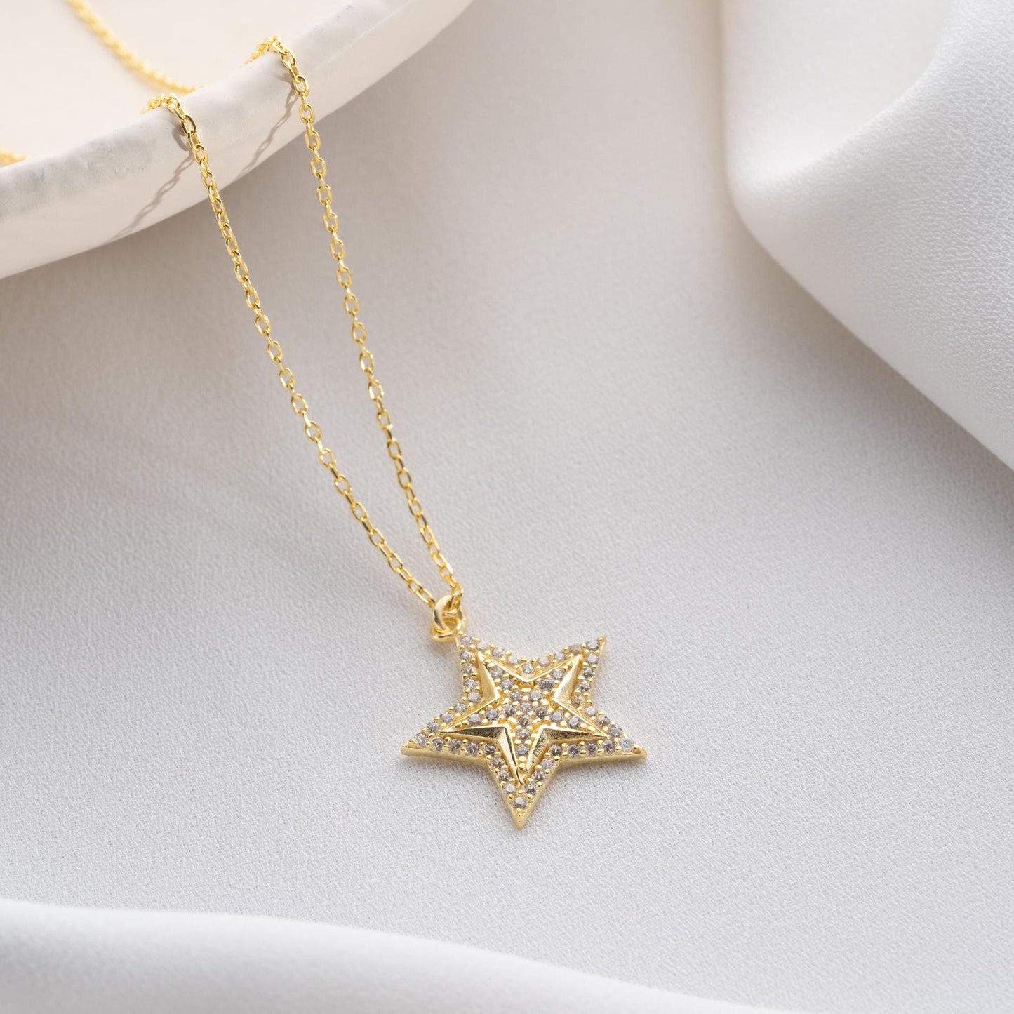 Star pendant necklace with cubic zirconia stones, available in 925 sterling silver and 14K gold plated options, displayed on a white satin background.