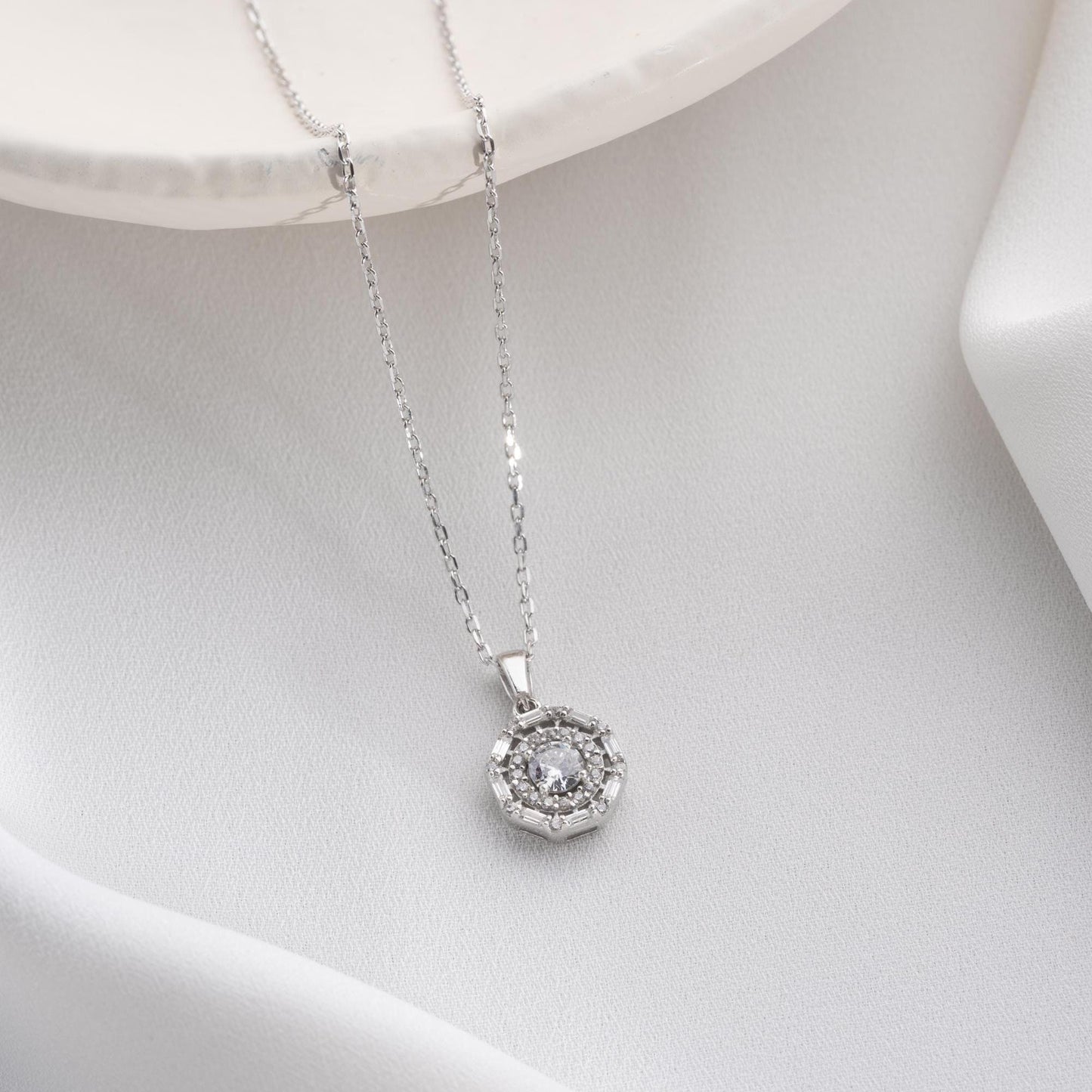 Halo pendant necklace with cubic zirconia stones, available in 925 sterling silver and 14K gold plated options, displayed on a white satin background.