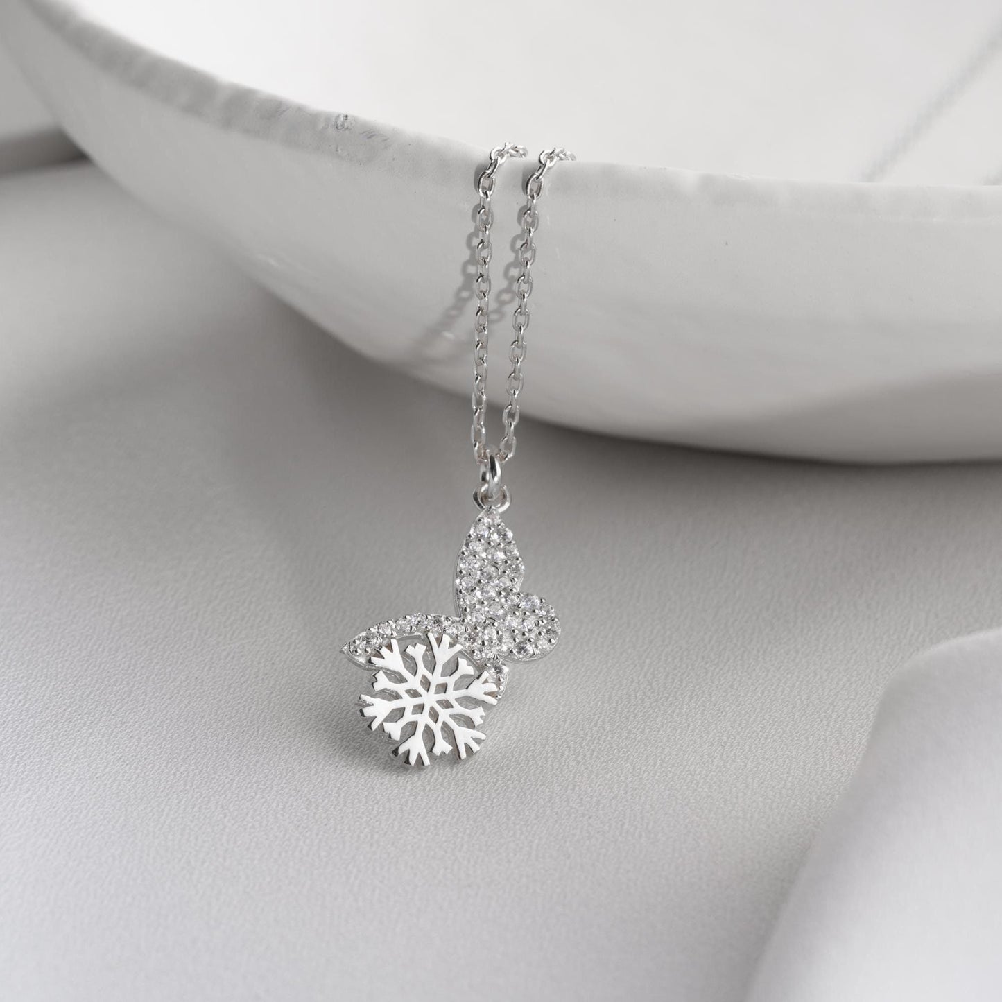 Snowflake heart necklace with cubic zirconia stones, available in 925 sterling silver and 14K gold plated options, displayed on a white satin background