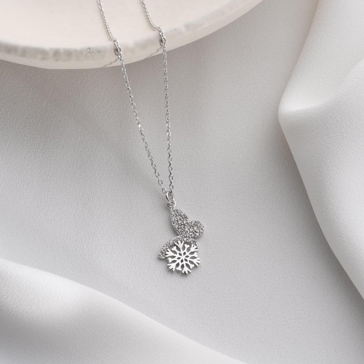 Snowflake heart necklace with cubic zirconia stones, available in 925 sterling silver and 14K gold plated options, displayed on a white satin background
