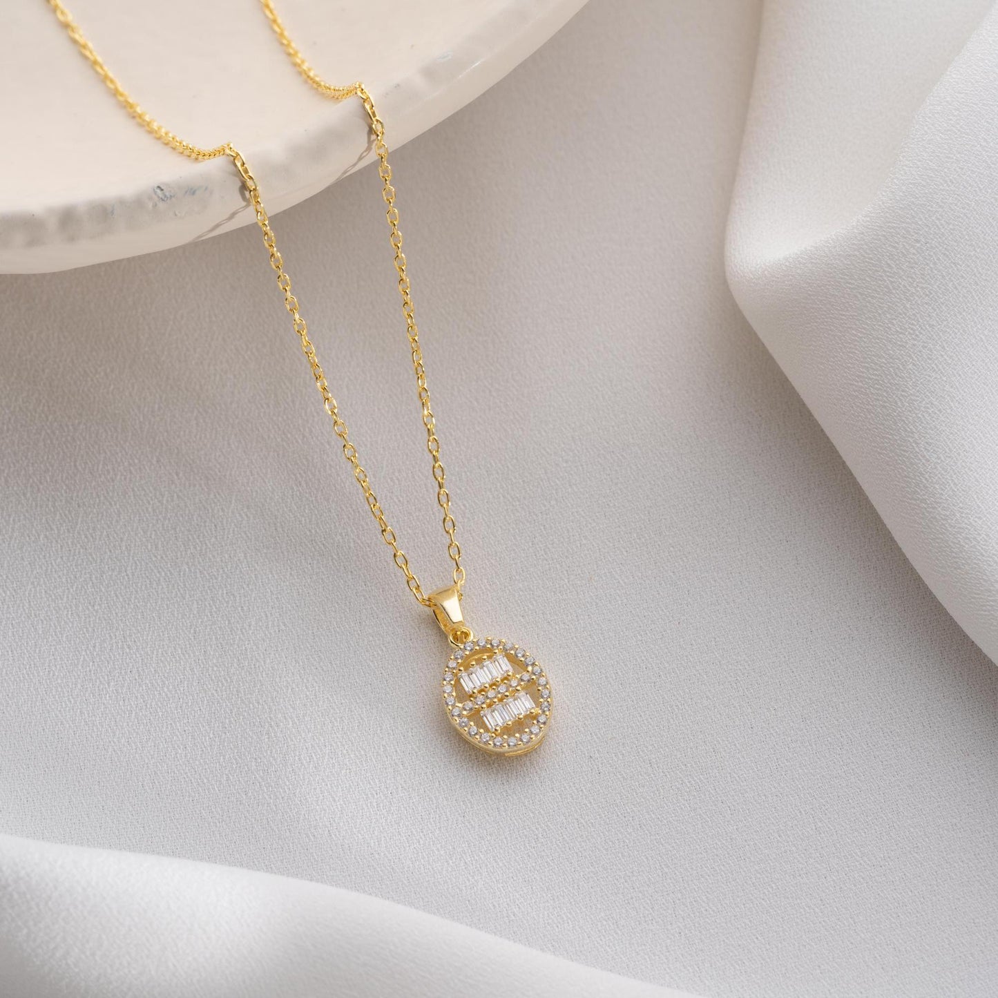 Oval pendant necklace with cubic zirconia stones, available in 925 sterling silver and 14K gold plated options, displayed on a white satin background