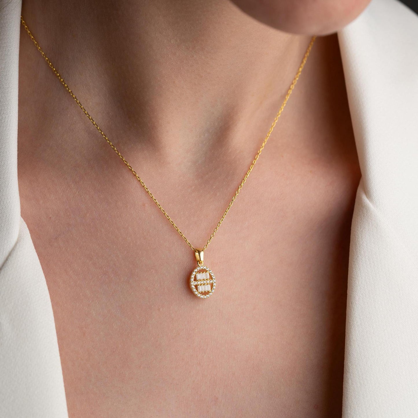 Oval pendant necklace with cubic zirconia stones, available in 925 sterling silver and 14K gold plated options, displayed on a white satin background
