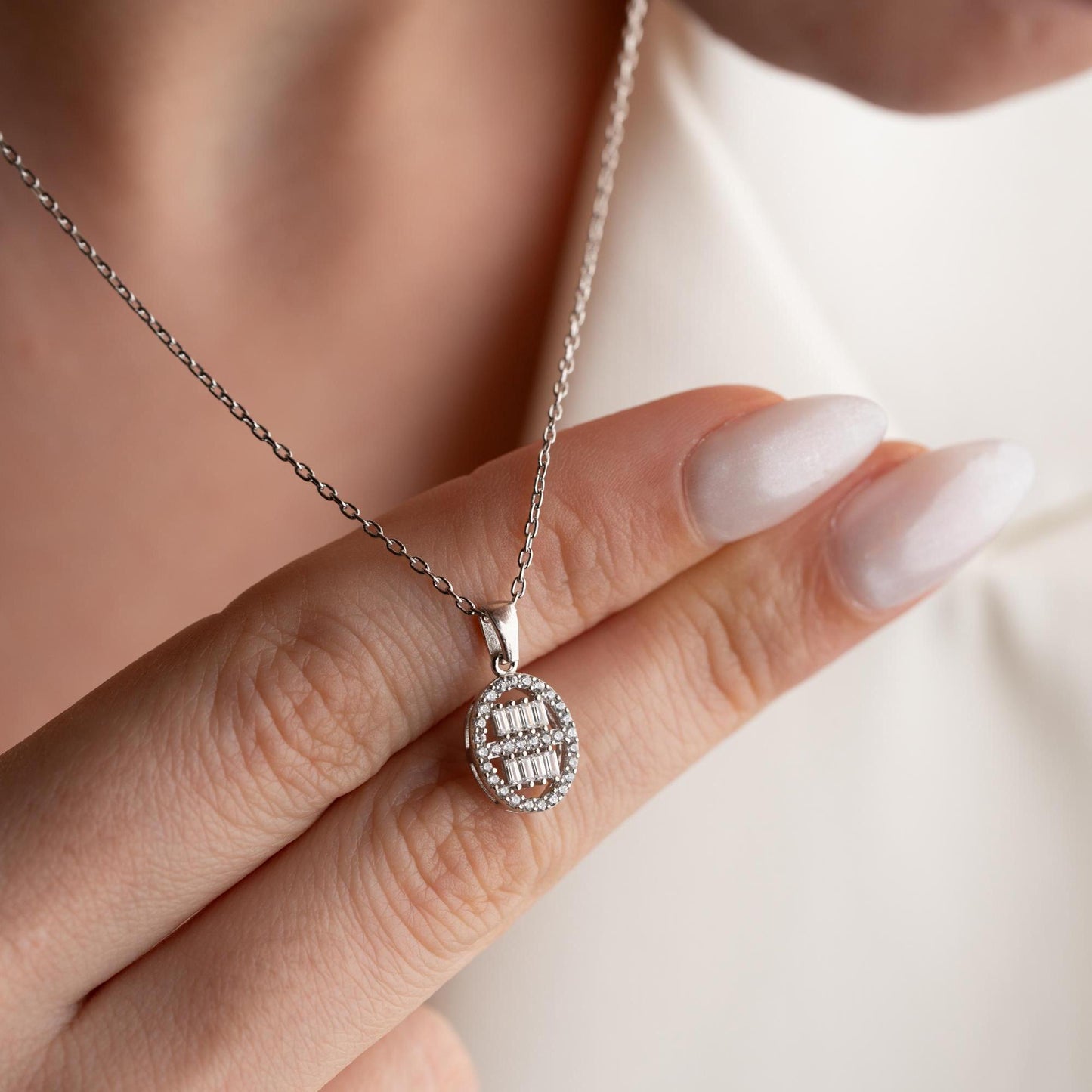 Oval pendant necklace with cubic zirconia stones, available in 925 sterling silver and 14K gold plated options, displayed on a white satin background