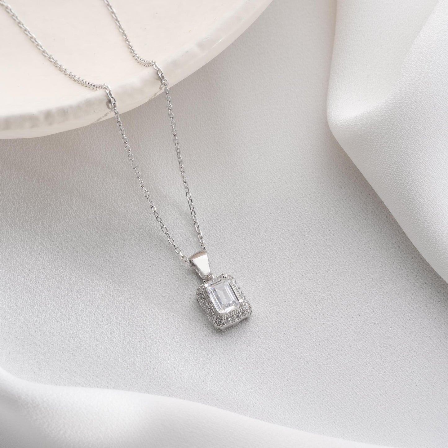 Emerald-cut pendant necklace with cubic zirconia stones, available in 925 sterling silver and 14K gold plated options, displayed on a white satin background.