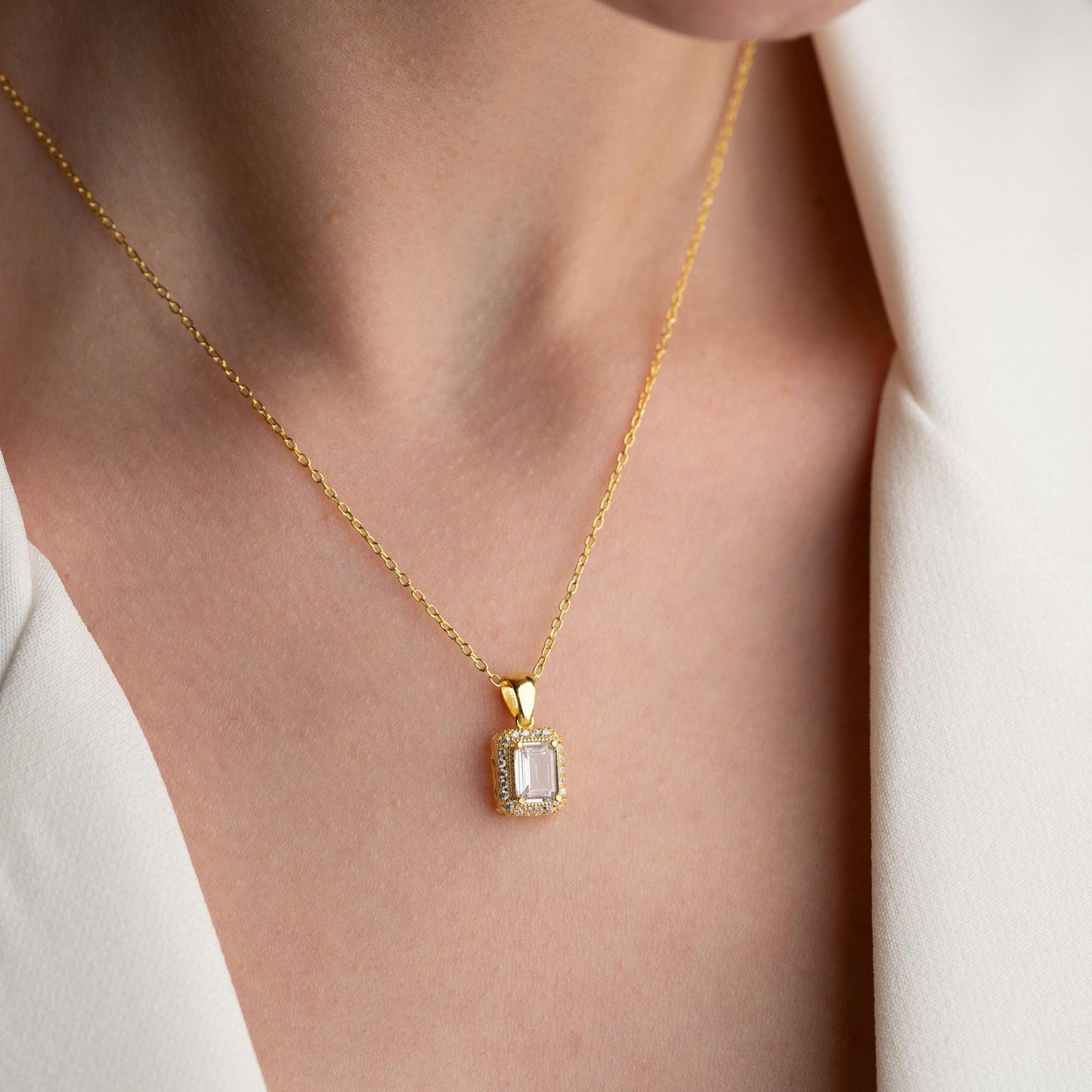 Emerald-cut pendant necklace with cubic zirconia stones, available in 925 sterling silver and 14K gold plated options, displayed on a white satin background.