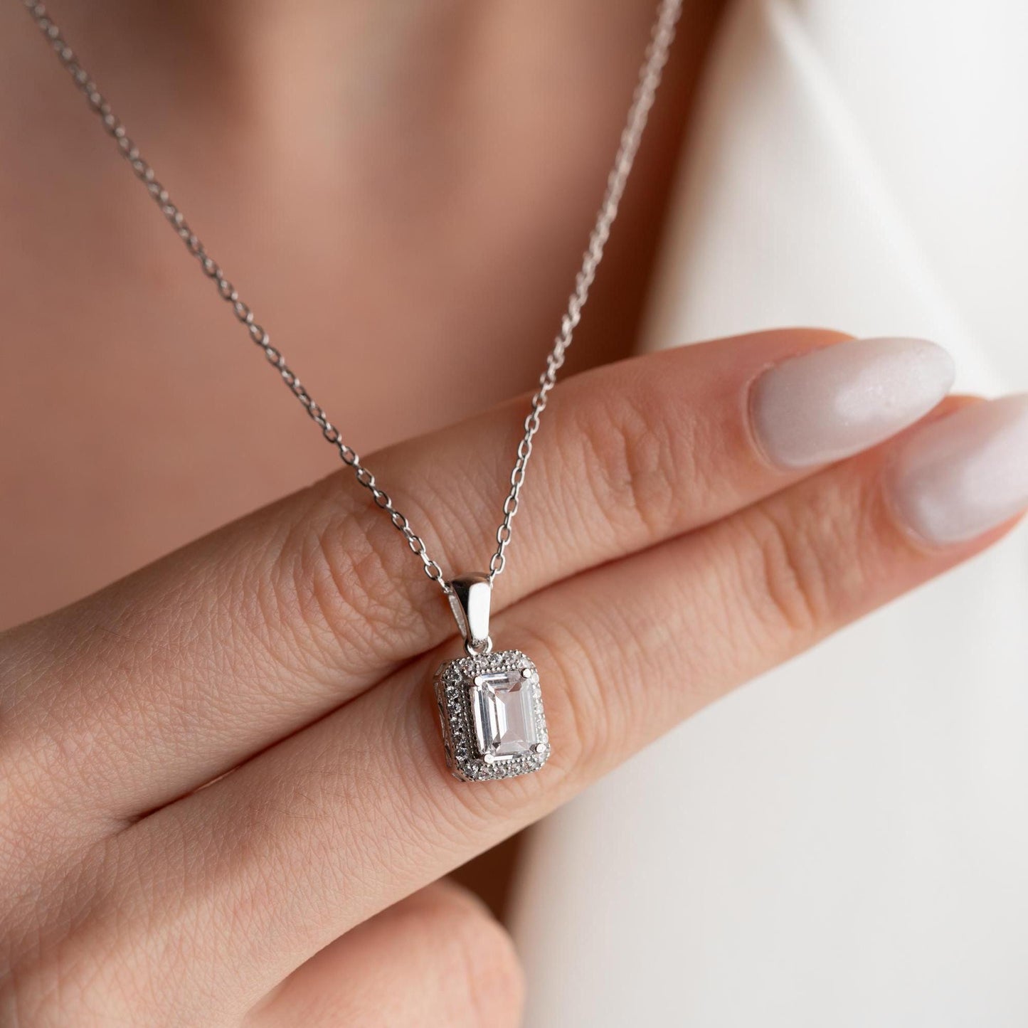 Emerald-cut pendant necklace with cubic zirconia stones, available in 925 sterling silver and 14K gold plated options, displayed on a white satin background.