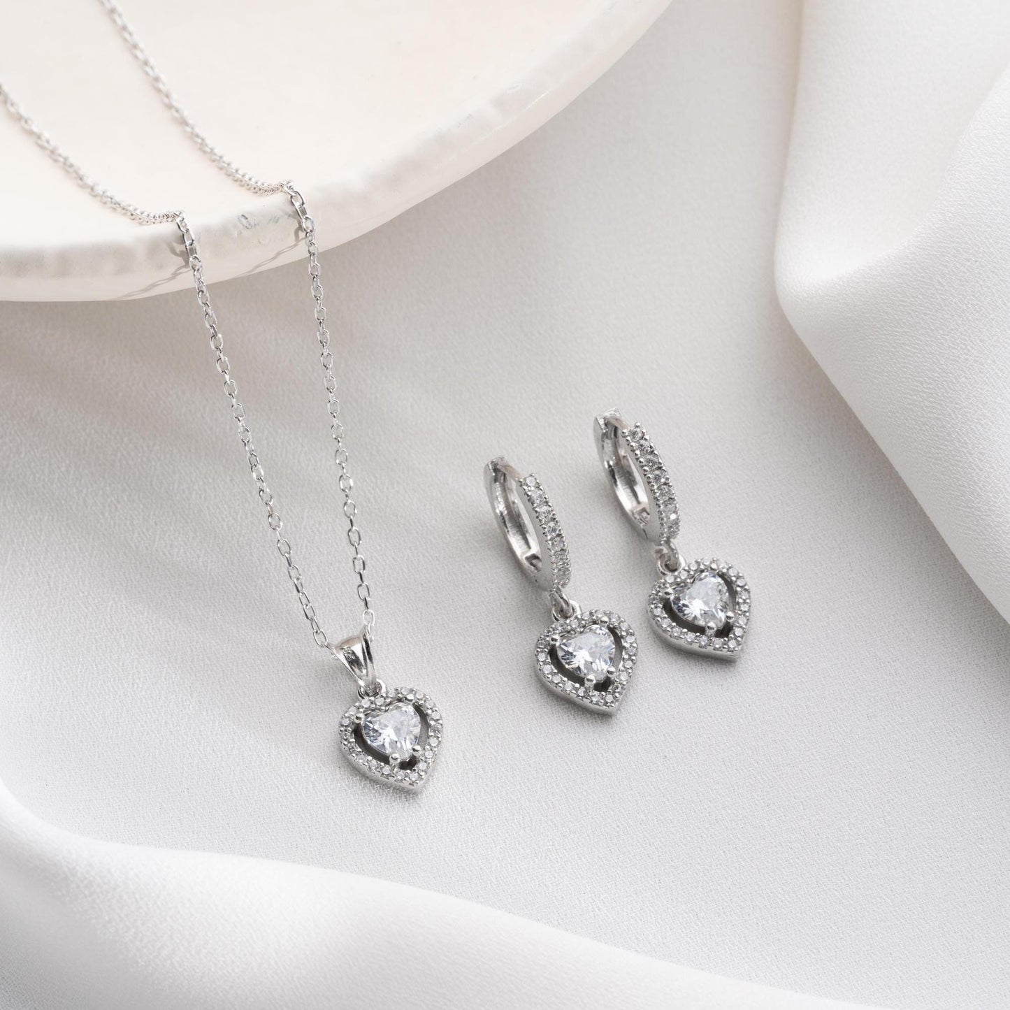 Heart pendant necklace and earrings set, crafted in 925 sterling silver with cubic zirconia stones, displayed on a soft satin background