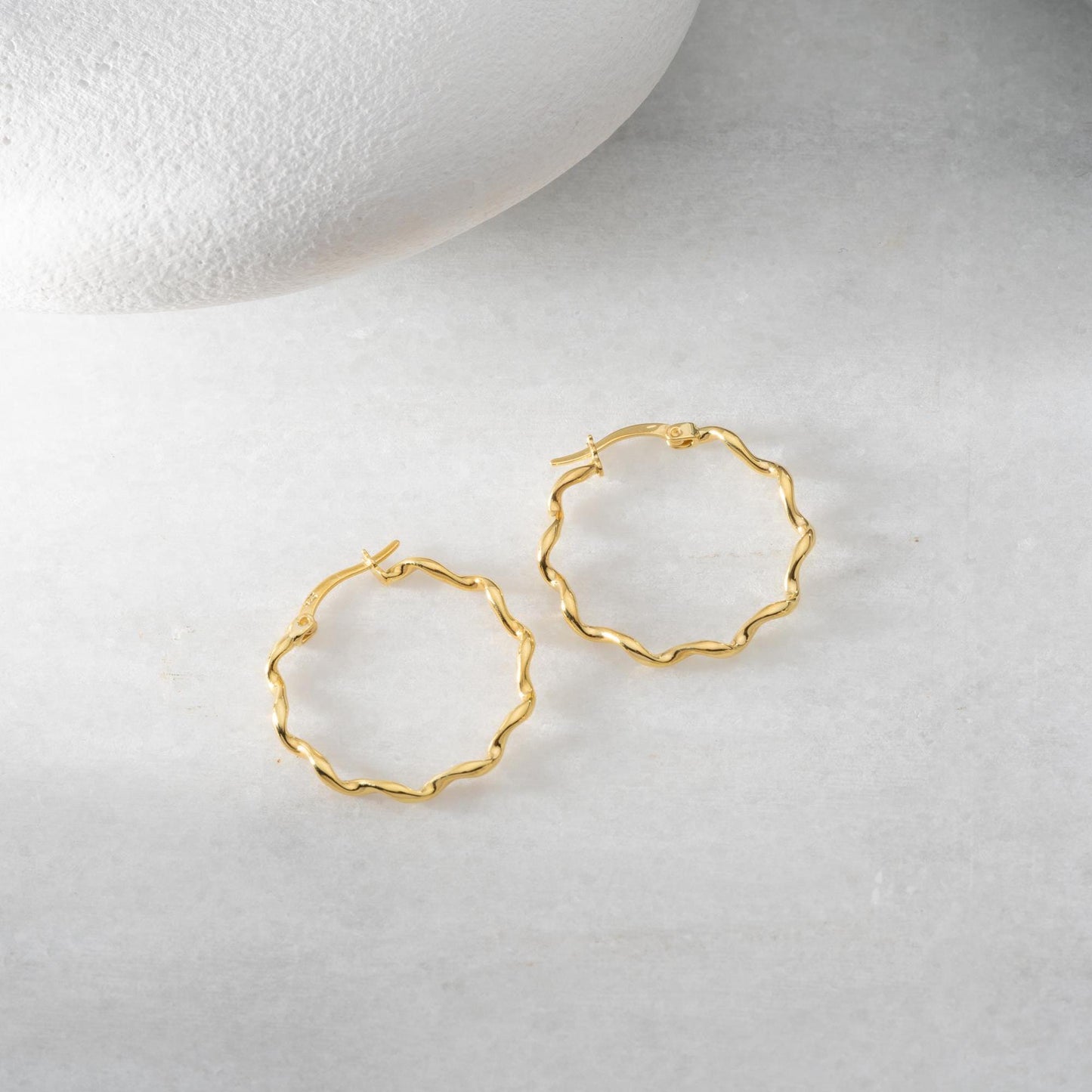 Wavy hoop earrings in 925 sterling silver and 14K gold plated options, displayed on a marble background