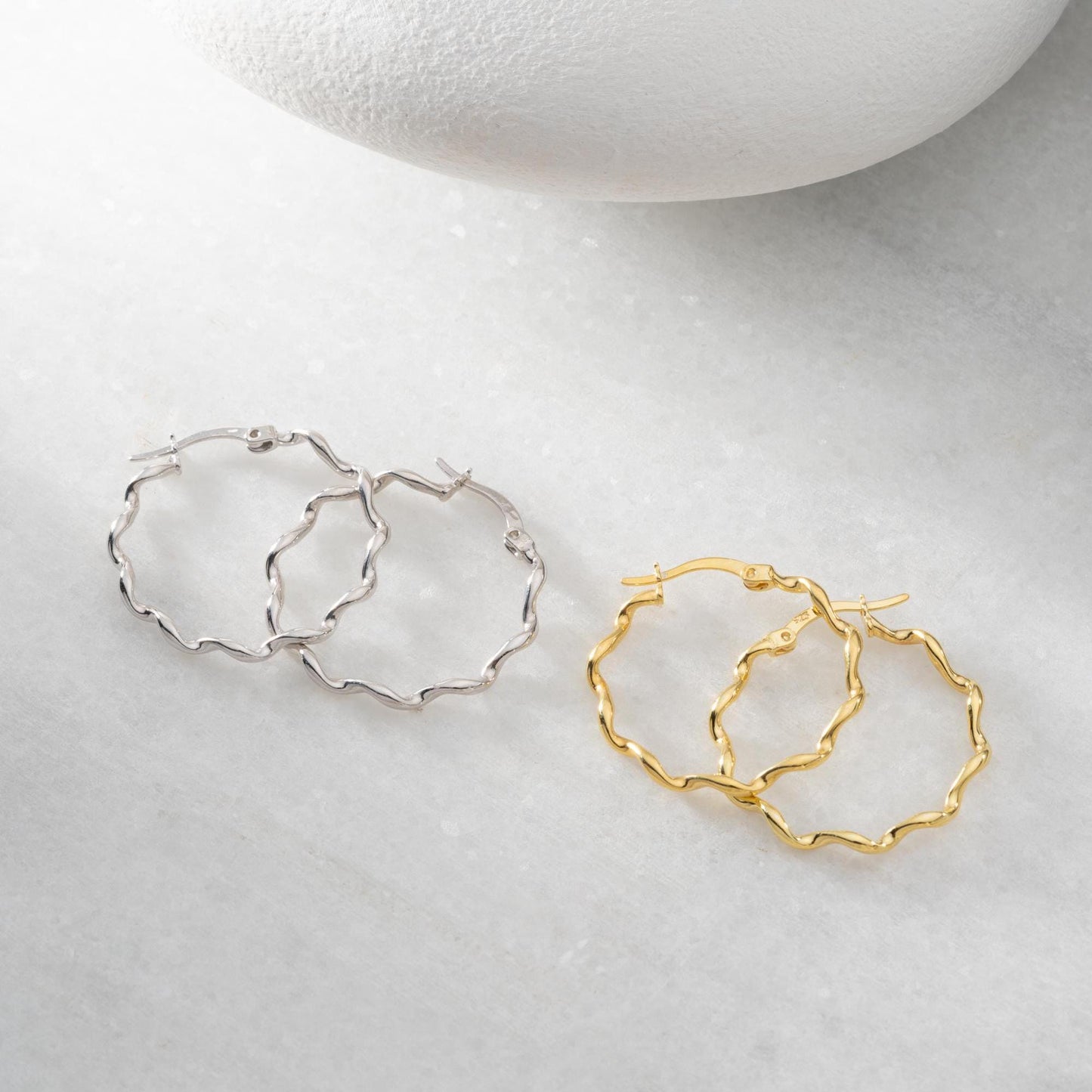 Wavy hoop earrings in 925 sterling silver and 14K gold plated options, displayed on a marble background