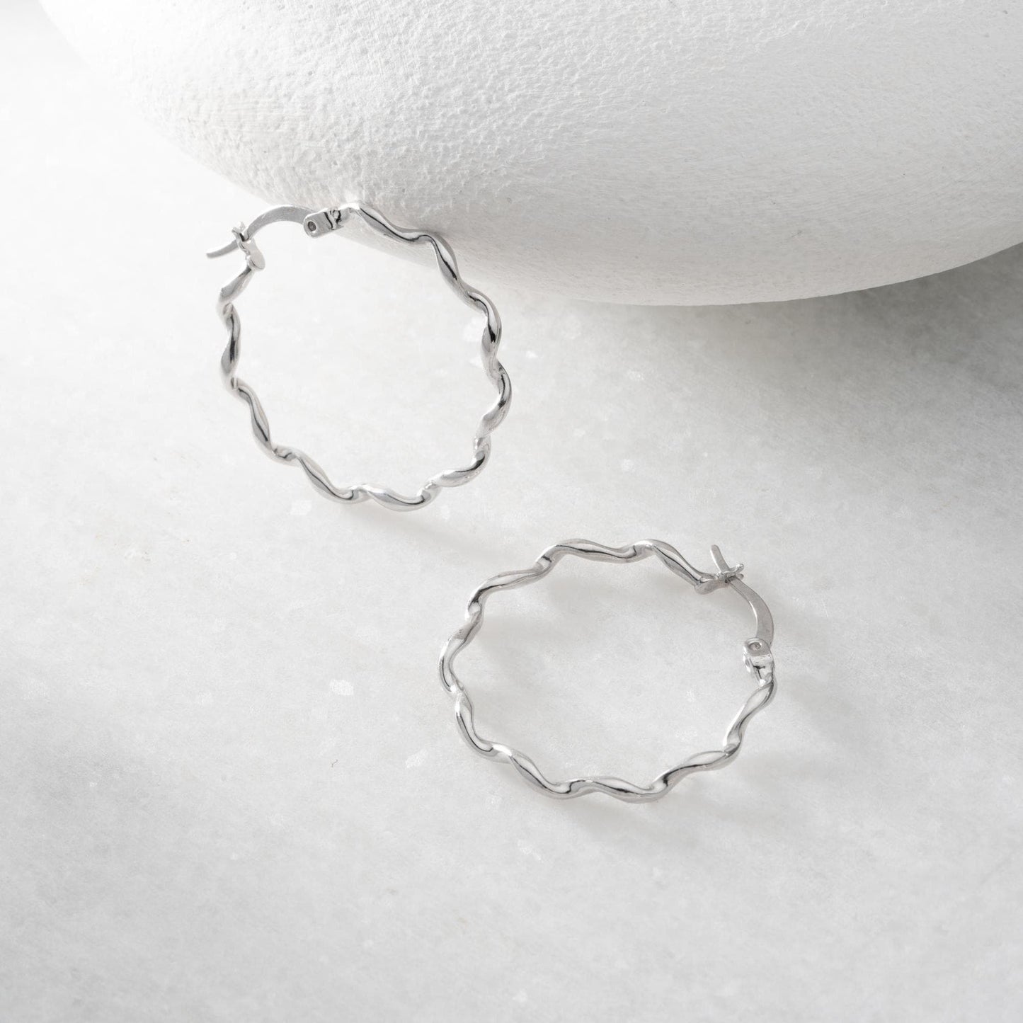 Wavy hoop earrings in 925 sterling silver and 14K gold plated options, displayed on a marble background