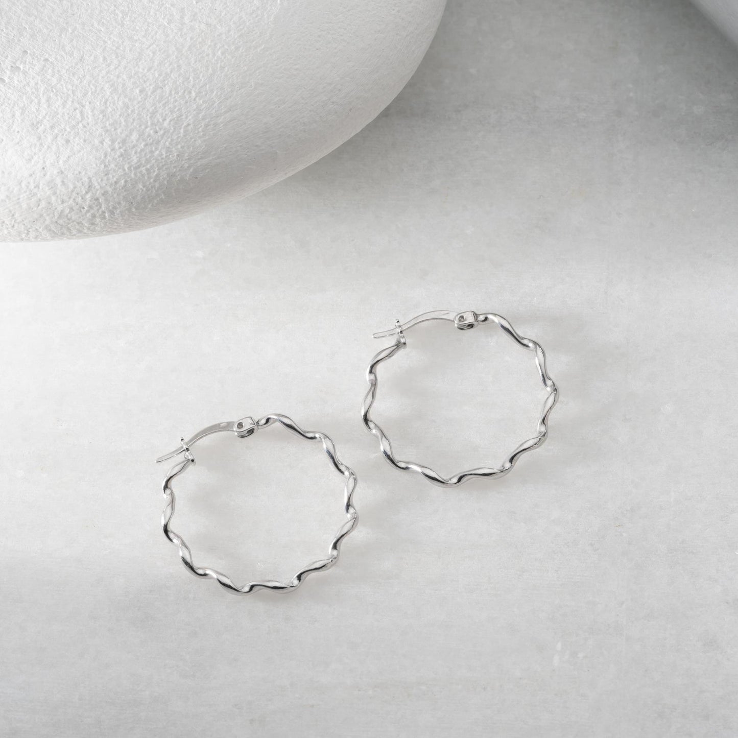 Wavy hoop earrings in 925 sterling silver and 14K gold plated options, displayed on a marble background