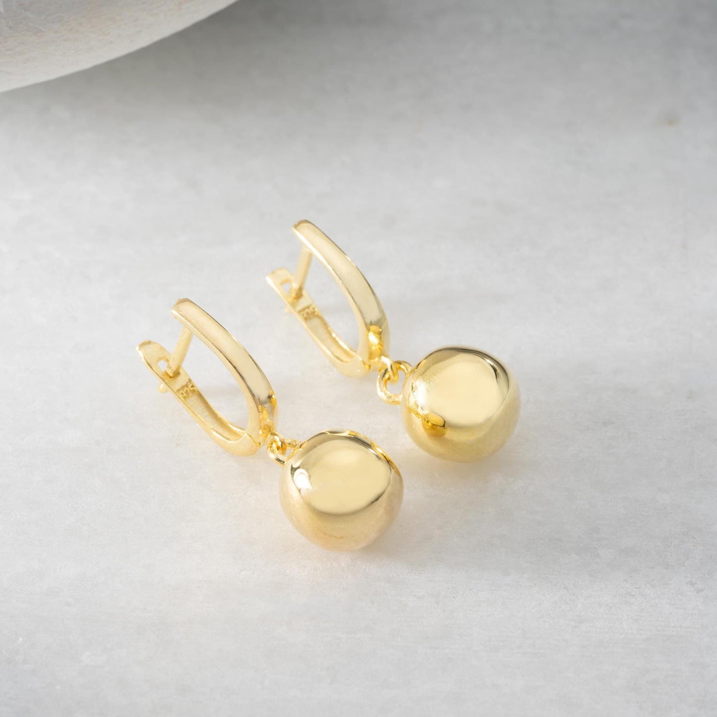 minimalist ball earrings in 925 sterling silver and 14K gold plated options, featuring a sleek design and lever-back closure displayed on a white marble background