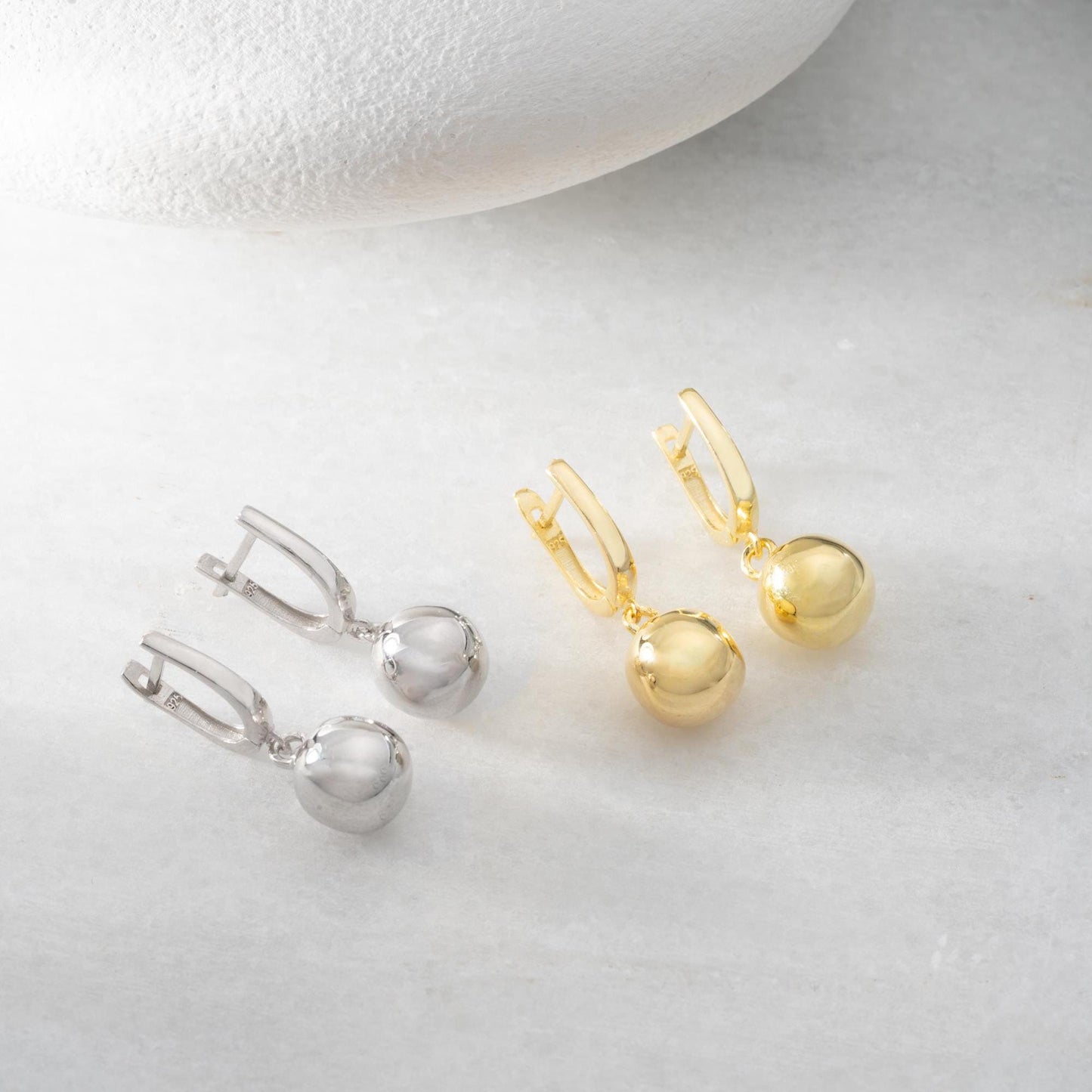 minimalist ball earrings in 925 sterling silver and 14K gold plated options, featuring a sleek design and lever-back closure displayed on a white marble background