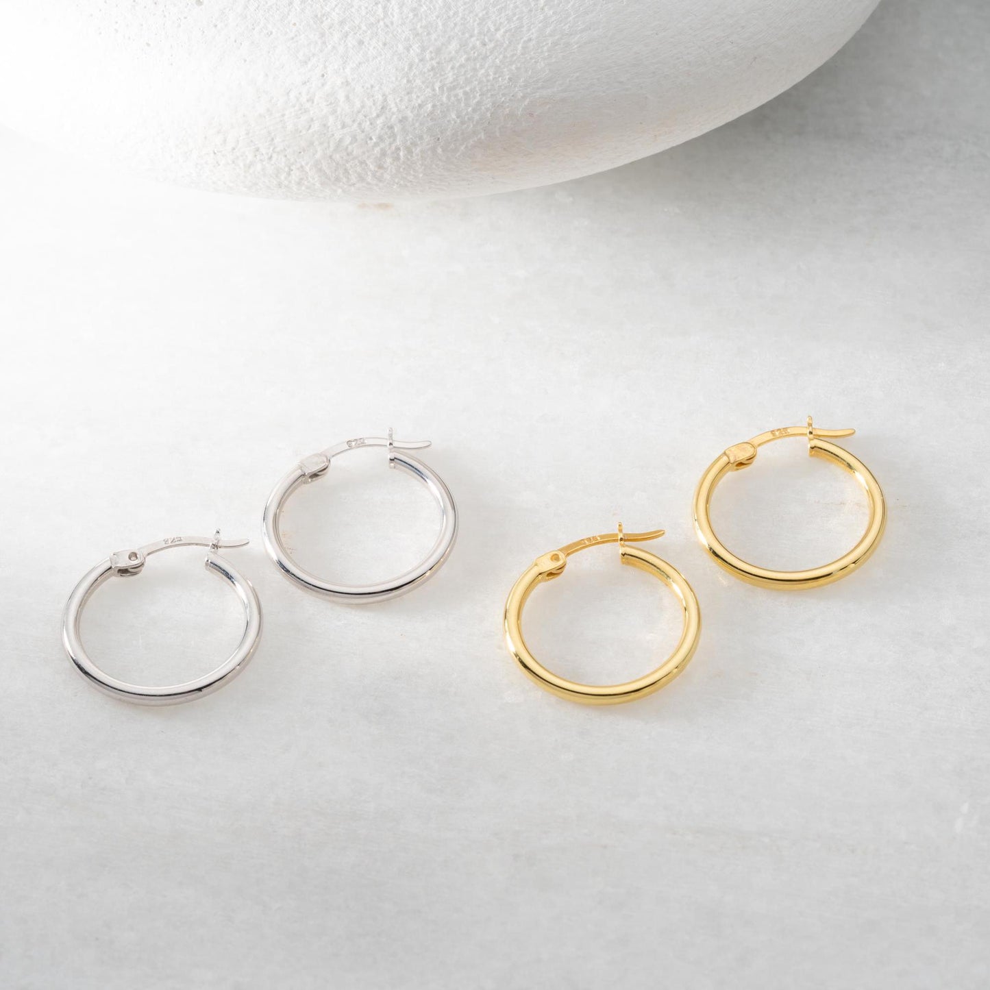 classic hoop earrings in 925 sterling silver and 14K gold plated options, featuring a minimalist polished design displayed on a marble background