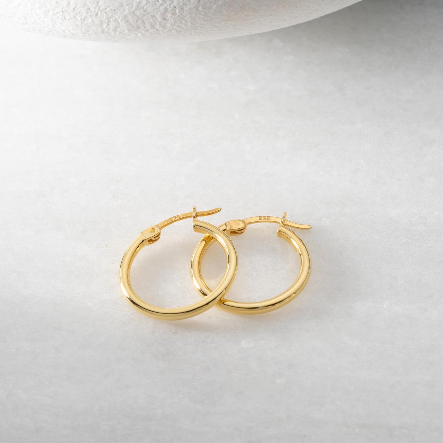 classic hoop earrings in 925 sterling silver and 14K gold plated options, featuring a minimalist polished design displayed on a marble background