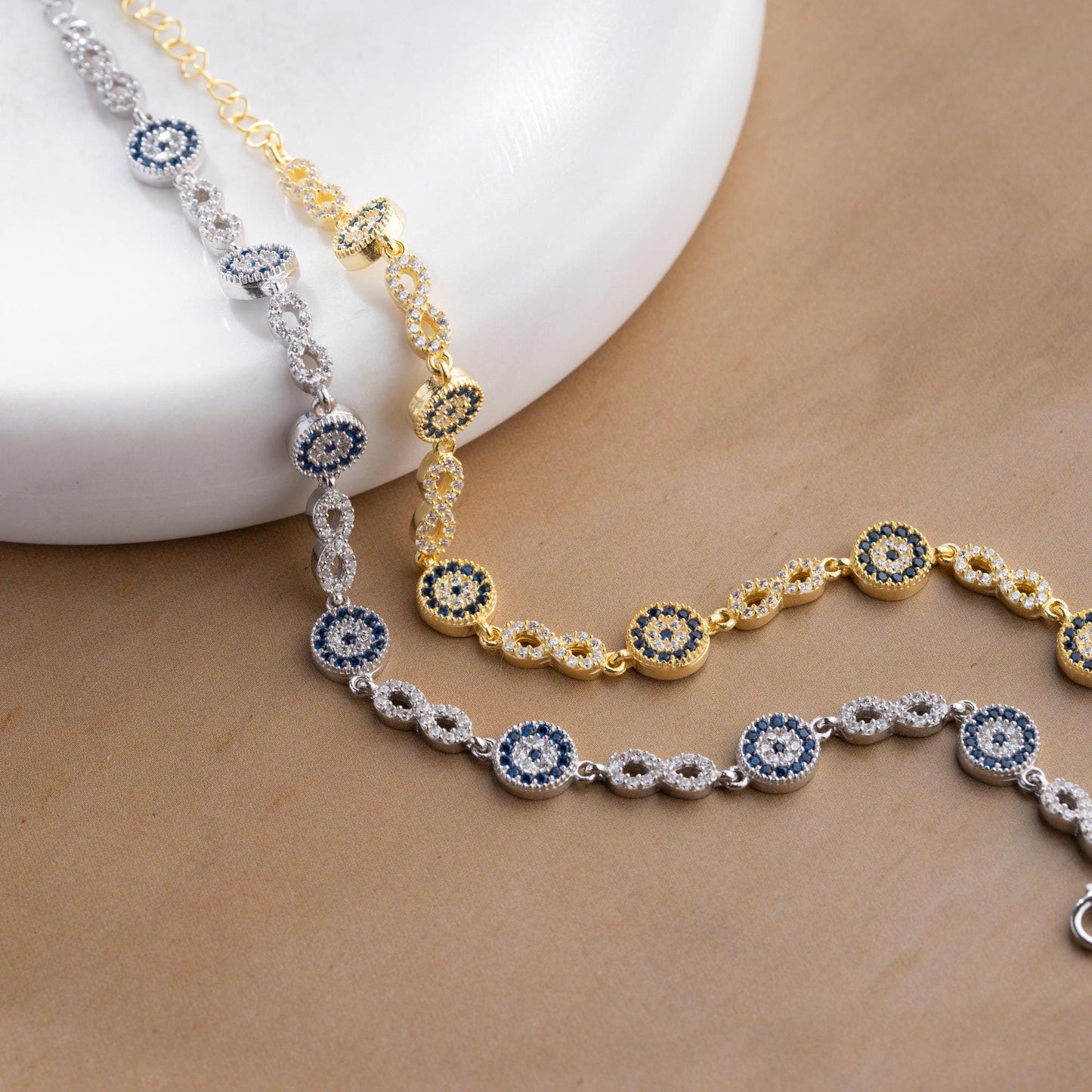 Infinity Evil Eye Bracelet with 925 Sterling Silver and 14K Gold Plated options, featuring blue evil eye accents, photographed in gold and silver variations.