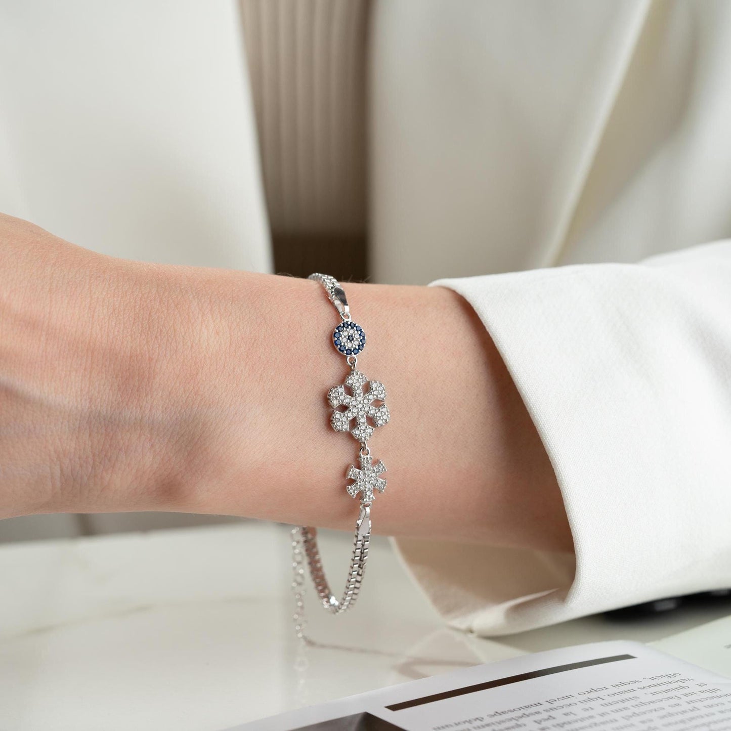 A stunning charm bracelet featuring delicate snowflake motifs and evil eye accents, crafted from 925 Sterling Silver and cubic zirconia stones, available in silver and gold finishes, ideal for festive gifting.