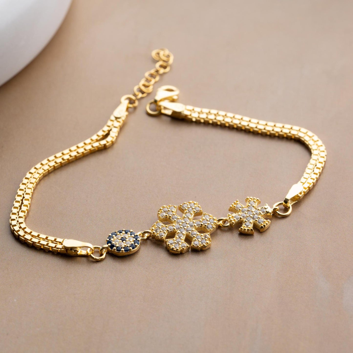 A stunning charm bracelet featuring delicate snowflake motifs and evil eye accents, crafted from 925 Sterling Silver and cubic zirconia stones, available in silver and gold finishes, ideal for festive gifting.