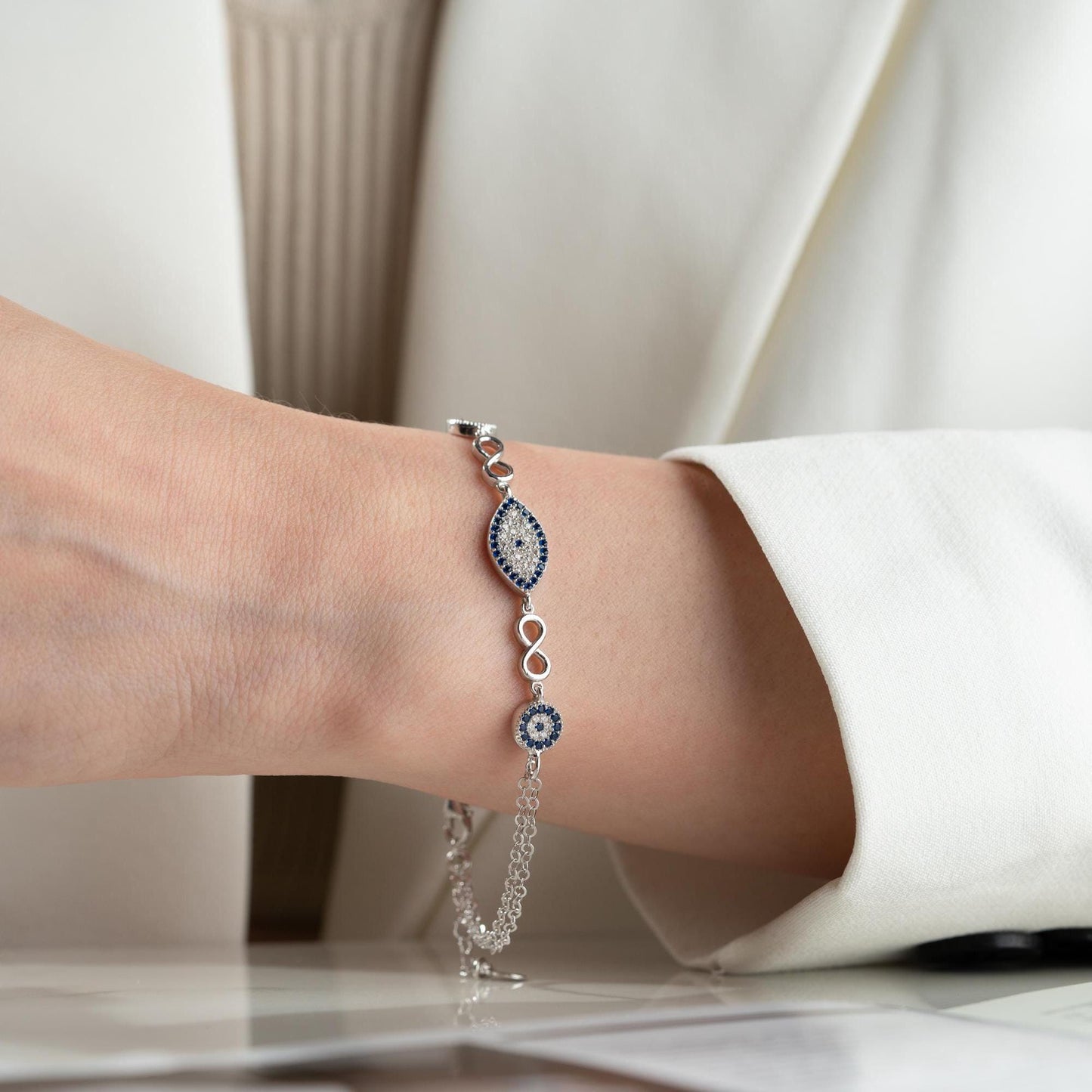 Elegant charm bracelet featuring evil eye and infinity symbols, crafted in 925 Sterling Silver with cubic zirconia stones, available in silver and gold finishes.