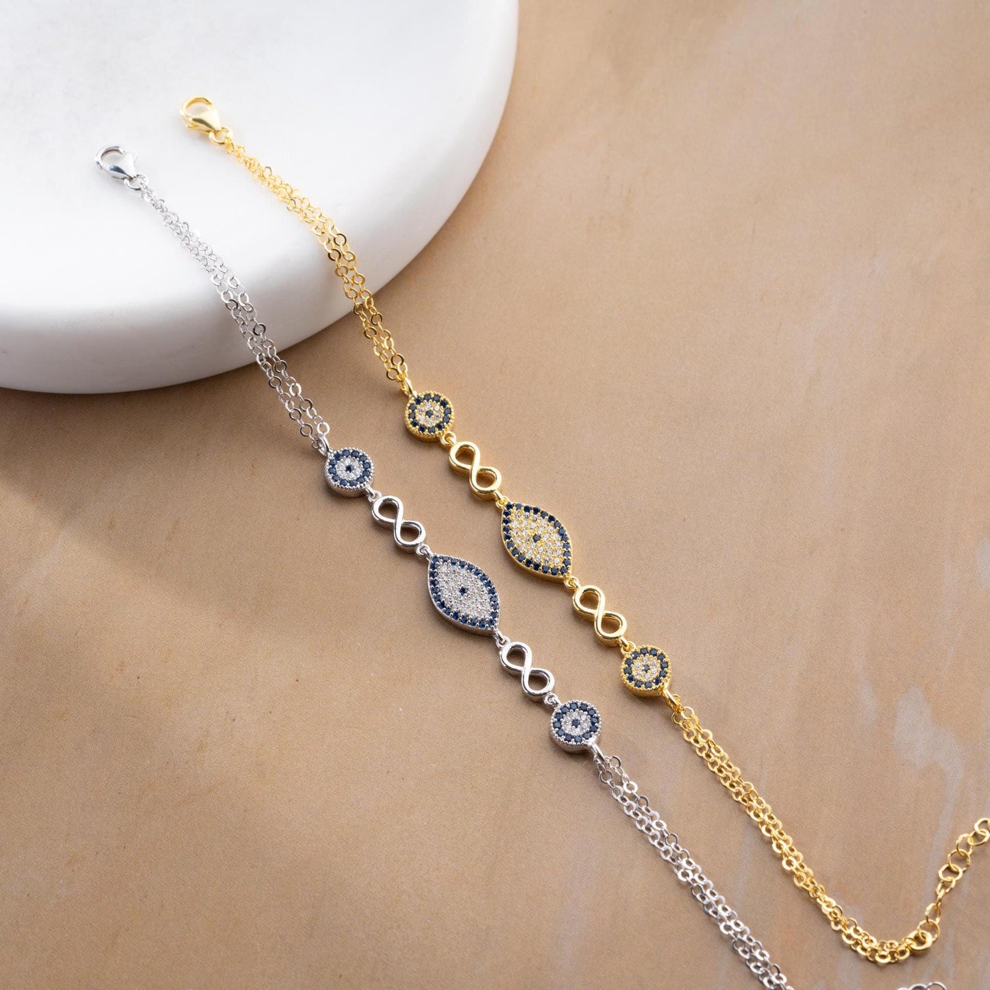 Elegant charm bracelet featuring evil eye and infinity symbols, crafted in 925 Sterling Silver with cubic zirconia stones, available in silver and gold finishes.