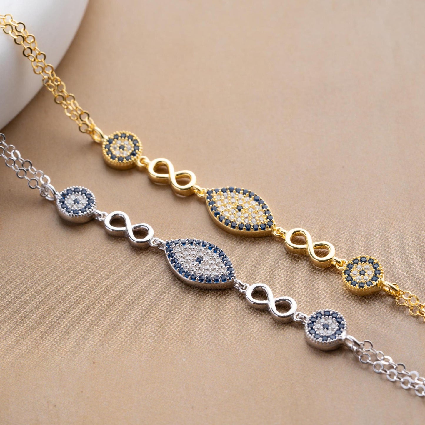 Elegant charm bracelet featuring evil eye and infinity symbols, crafted in 925 Sterling Silver with cubic zirconia stones, available in silver and gold finishes.