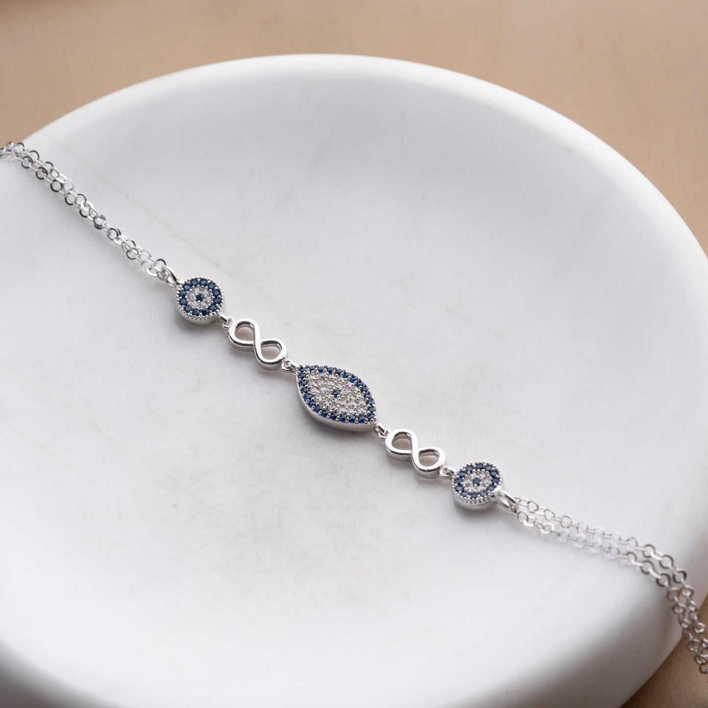 Elegant charm bracelet featuring evil eye and infinity symbols, crafted in 925 Sterling Silver with cubic zirconia stones, available in silver and gold finishes.