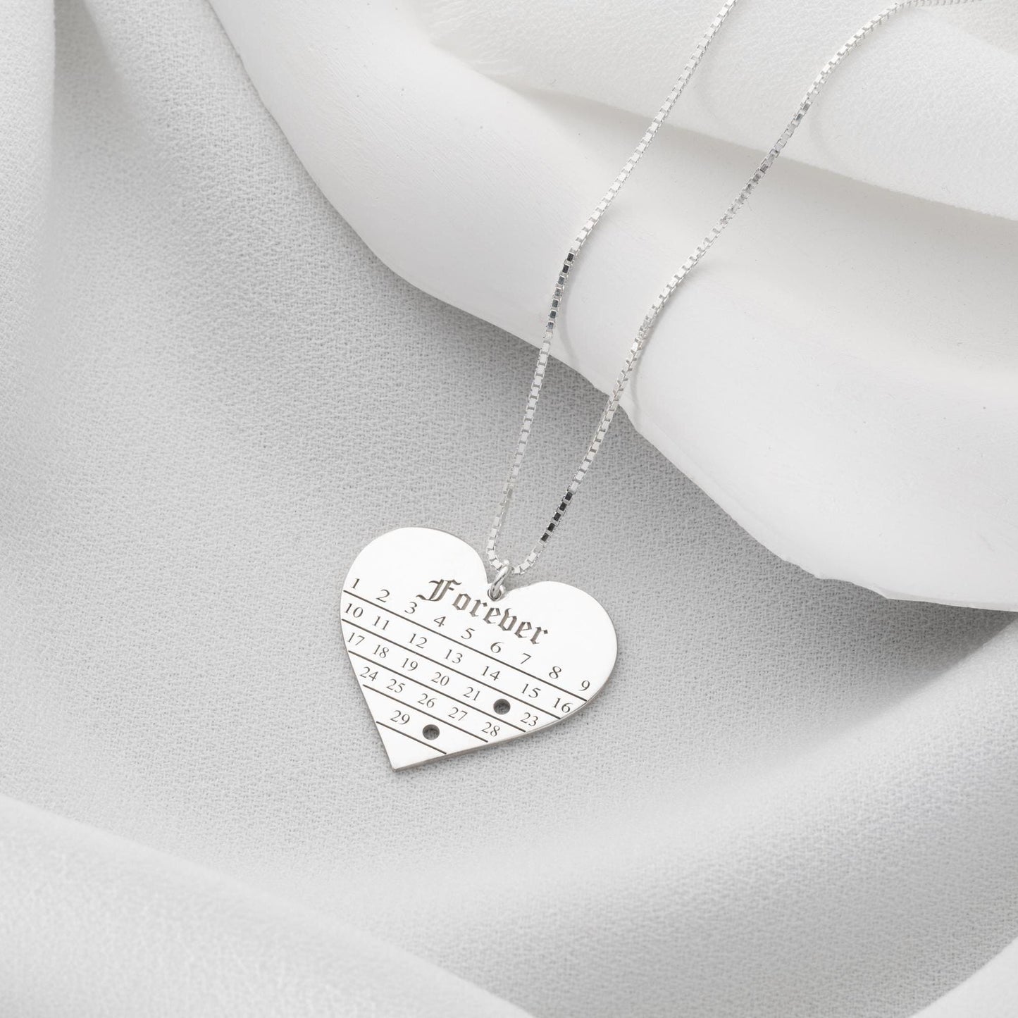 A personalized heart-shaped calendar necklace with a custom date engraving, available in sterling silver and gold plated finishes. Perfect for anniversaries, weddings, or Valentine's Day.