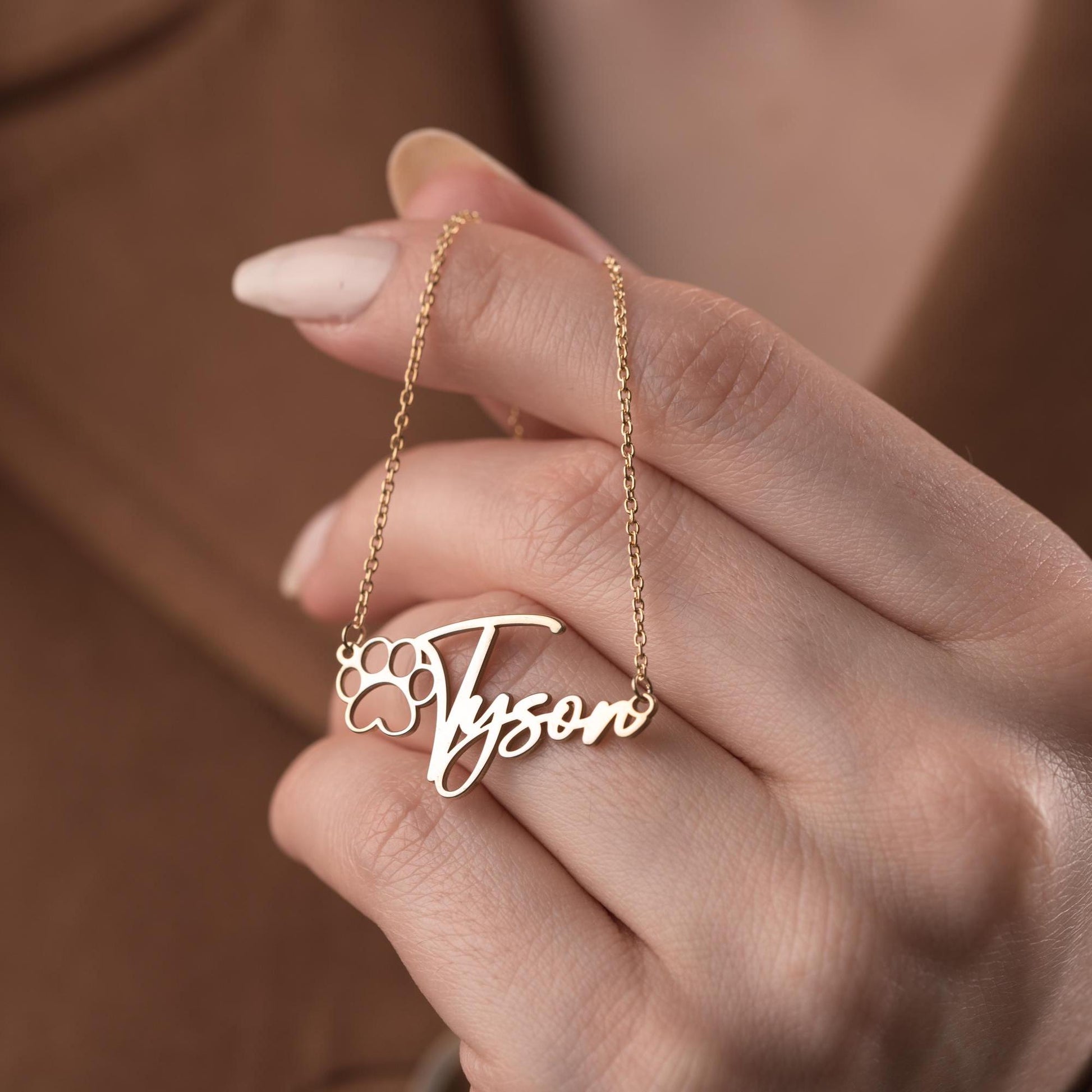 Custom pet name necklace with a paw print design in 925 sterling silver and 14k gold plated options, perfect for pet lovers. A personalized, handmade gift displayed on a soft fabric background.