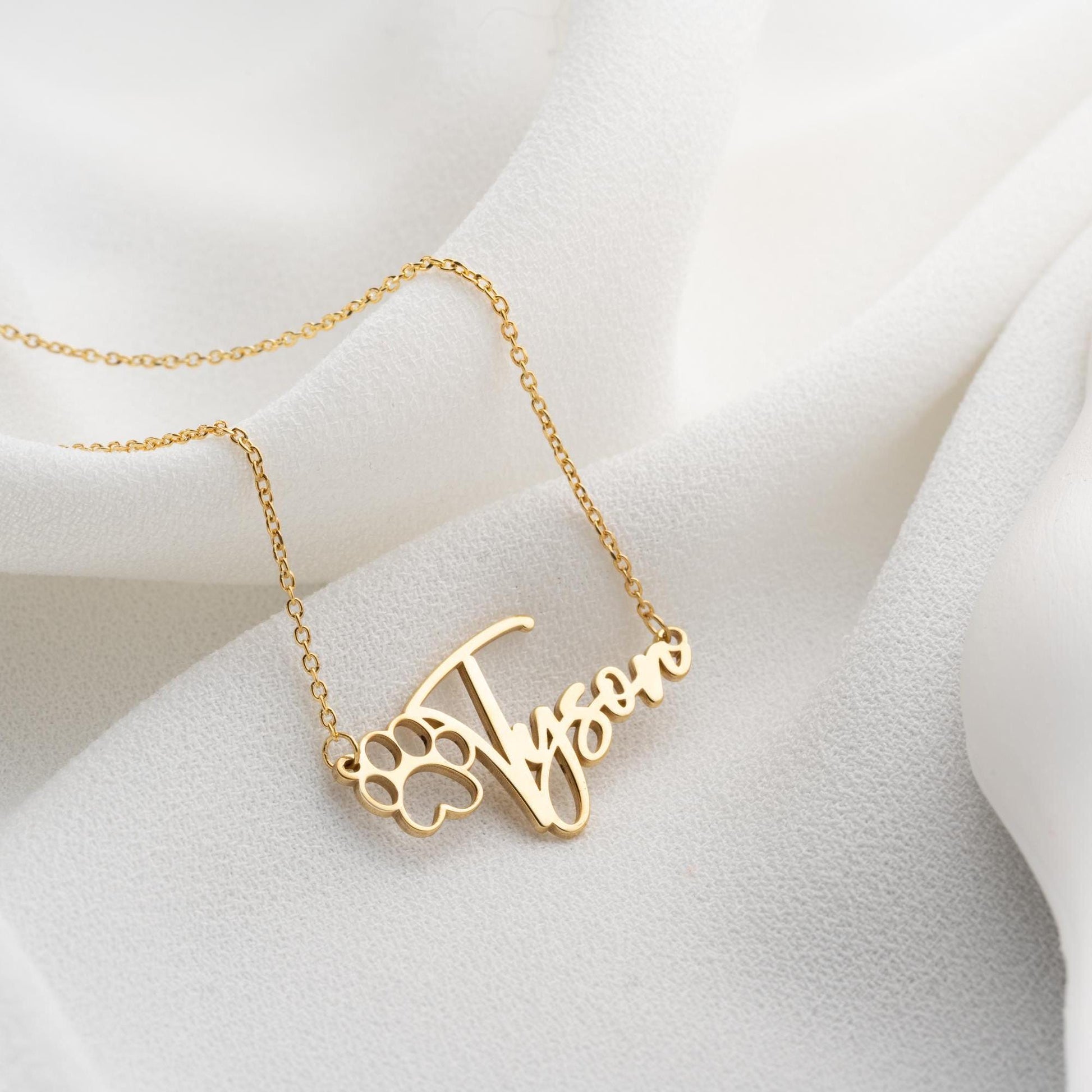 Custom pet name necklace with a paw print design in 925 sterling silver and 14k gold plated options, perfect for pet lovers. A personalized, handmade gift displayed on a soft fabric background.