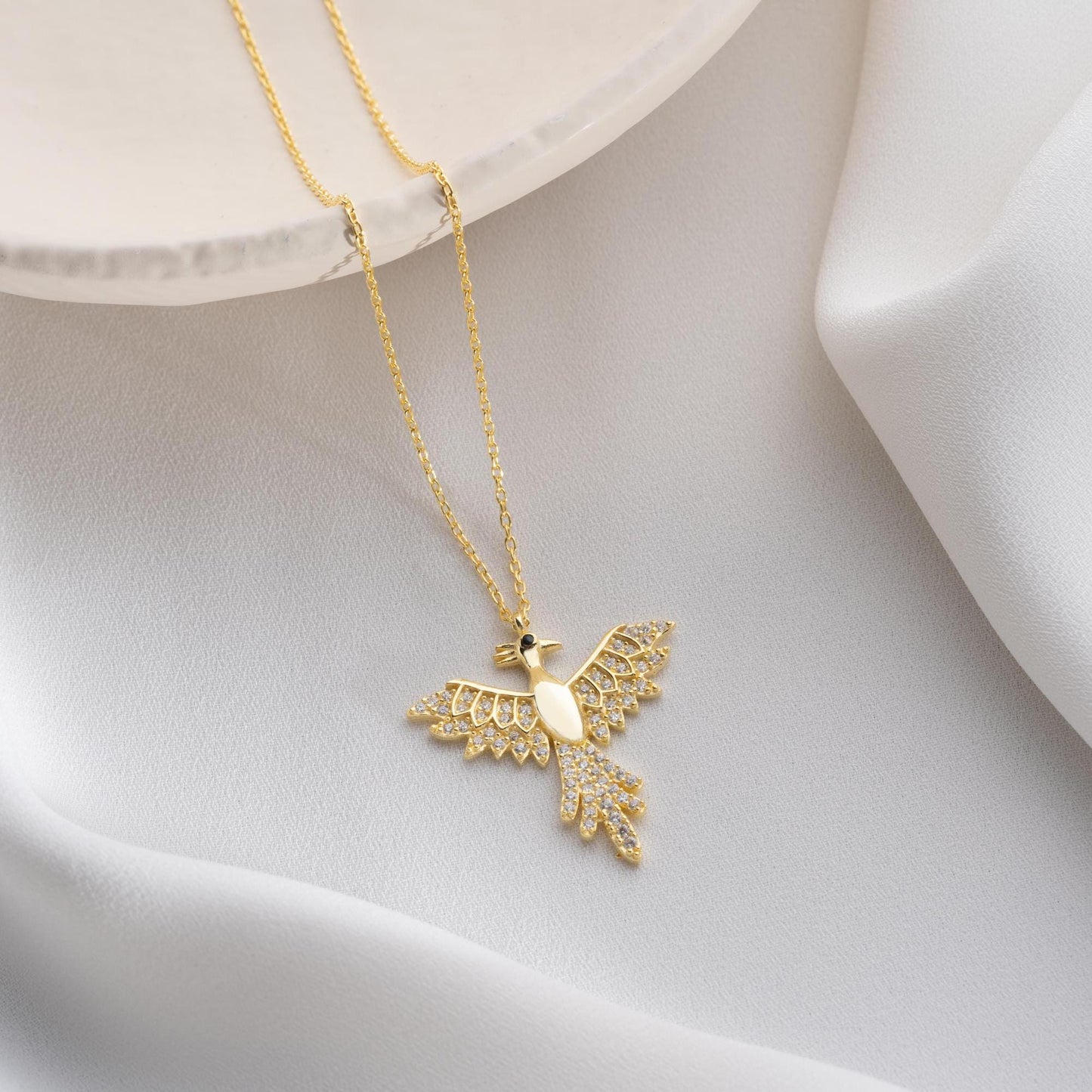 Elegant bird-shaped necklace with cubic zirconia stones, available in 925 sterling silver and 14K gold plated options, displayed on a white satin background.