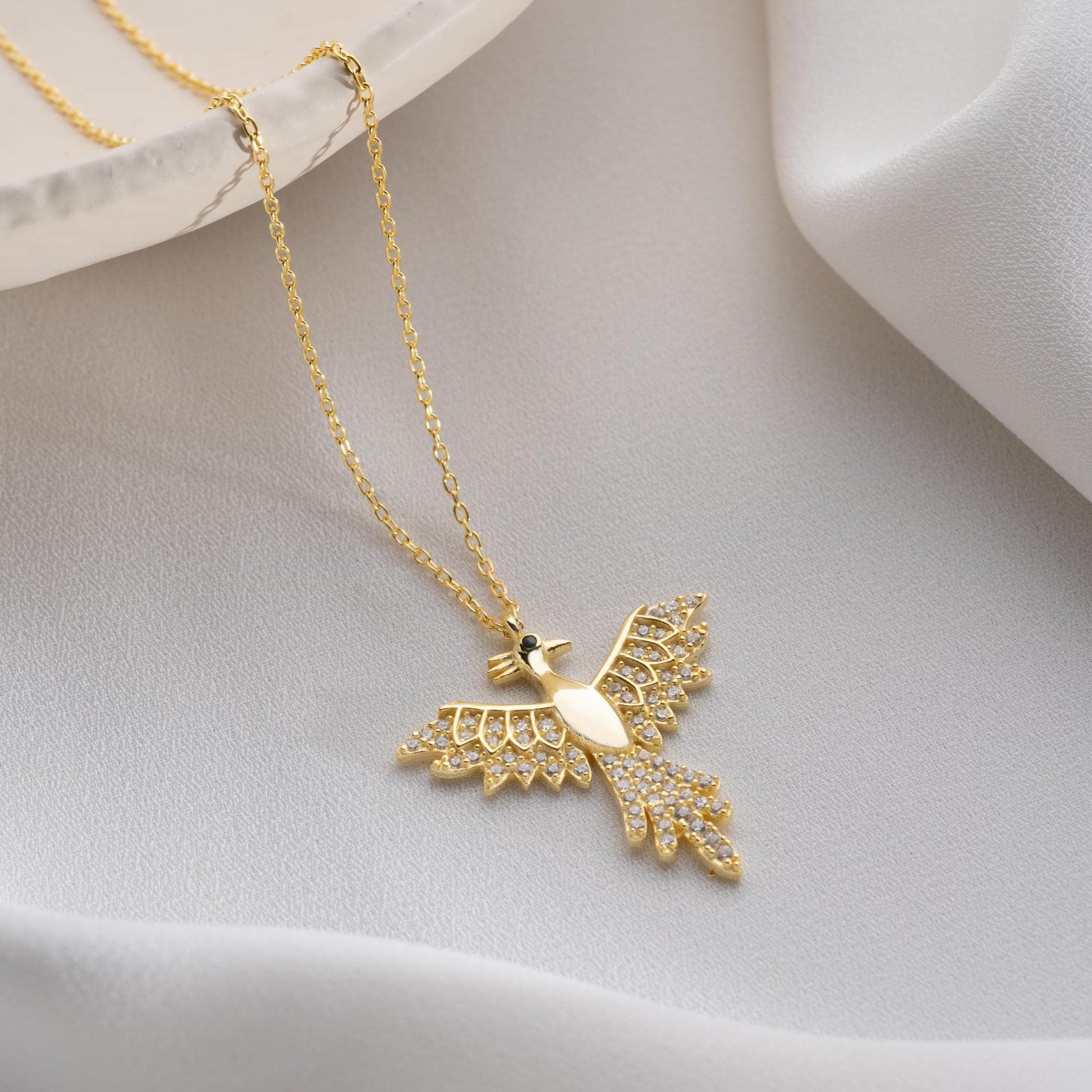 Elegant bird-shaped necklace with cubic zirconia stones, available in 925 sterling silver and 14K gold plated options, displayed on a white satin background.