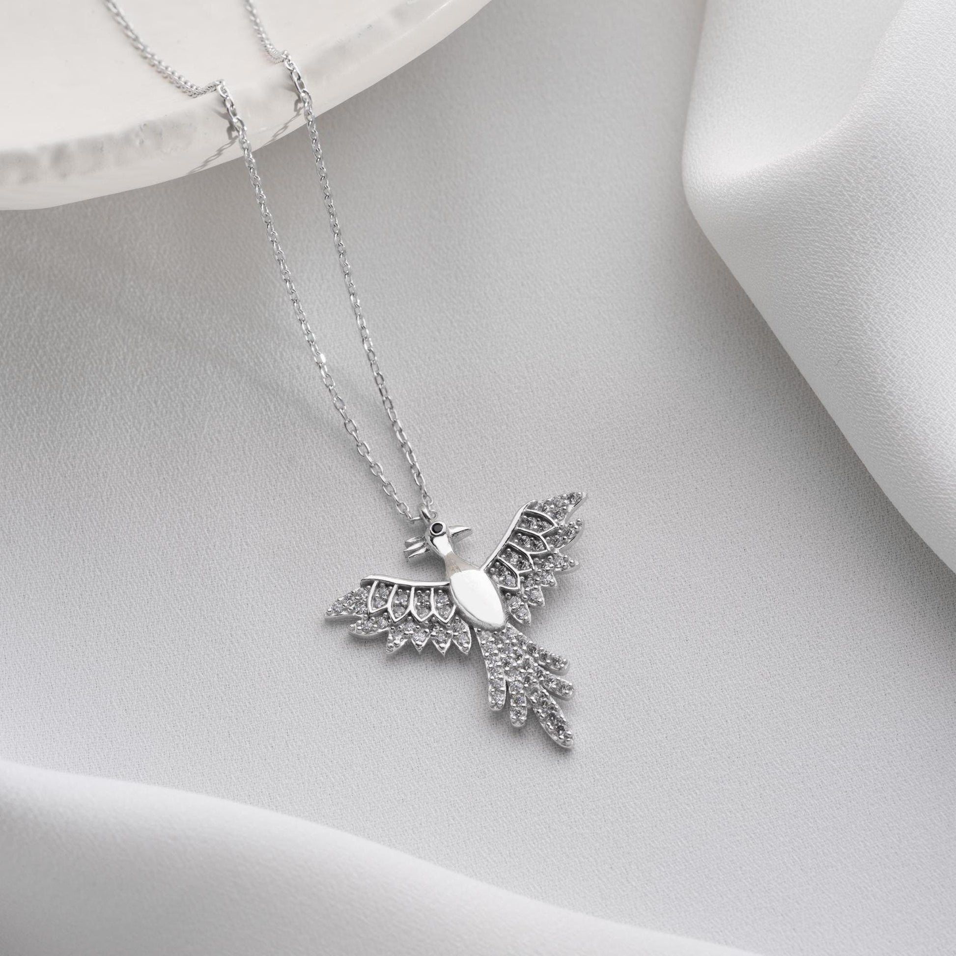 Elegant bird-shaped necklace with cubic zirconia stones, available in 925 sterling silver and 14K gold plated options, displayed on a white satin background.