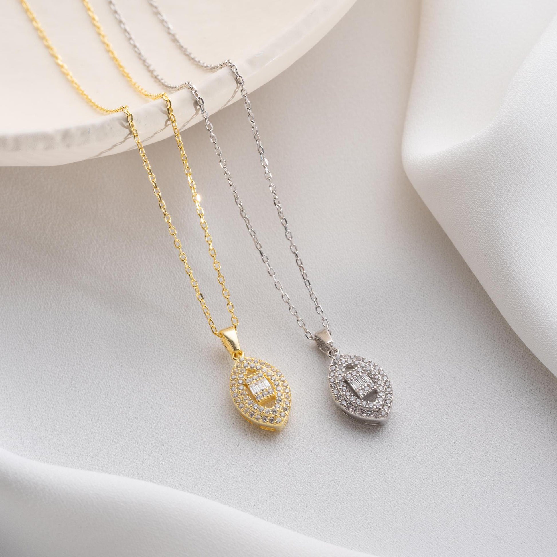 Elegant oval pendant necklace with cubic zirconia stones, available in 925 sterling silver and 14K gold plated options, displayed on a white satin background.